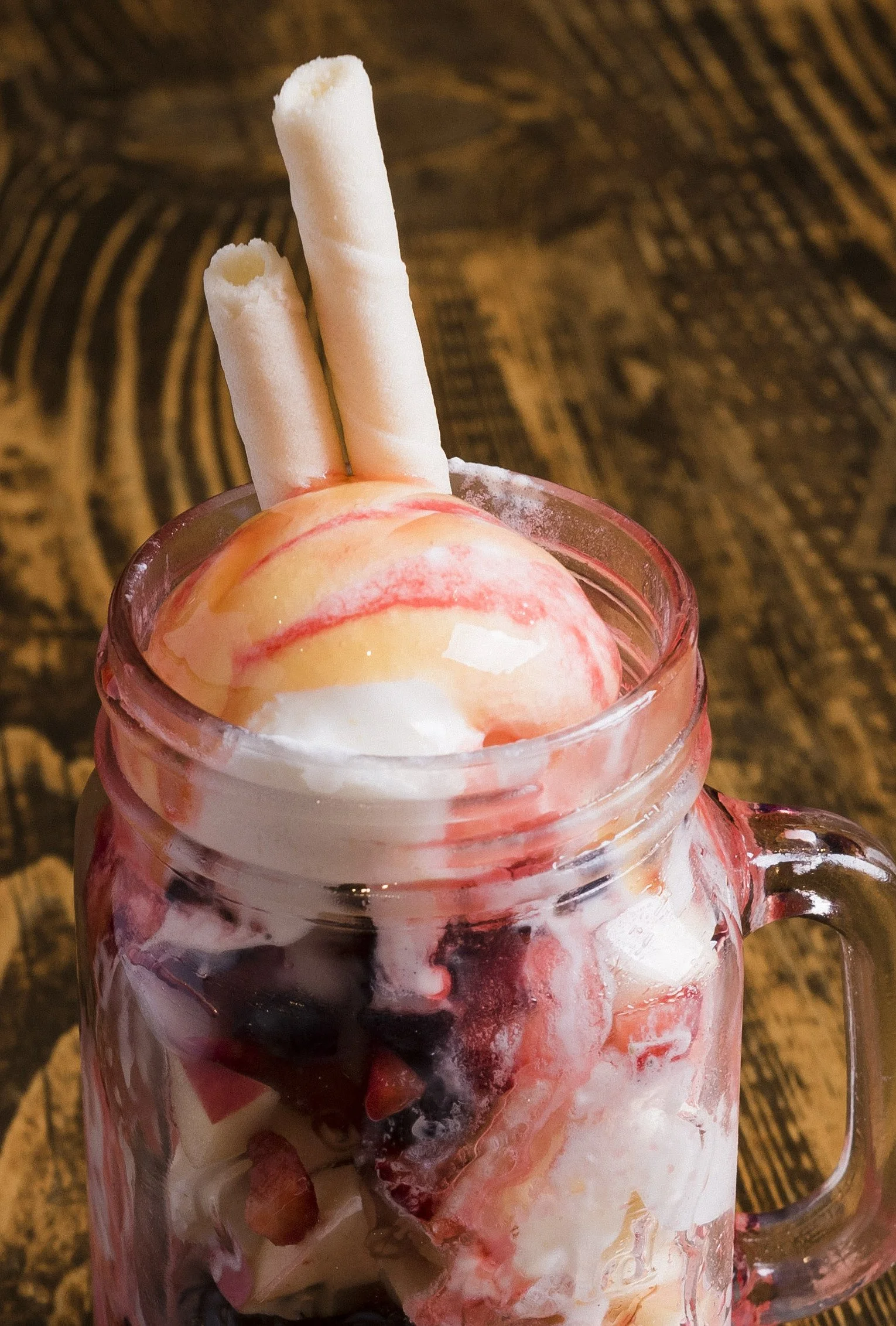 A dessert in a glass jar topped with peach ice cream, whipped cream, and rolled wafer cookies.