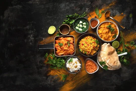 Assorted Indian dishes including curry, rice, naan bread, chutneys, and garnishes on a dark surface.