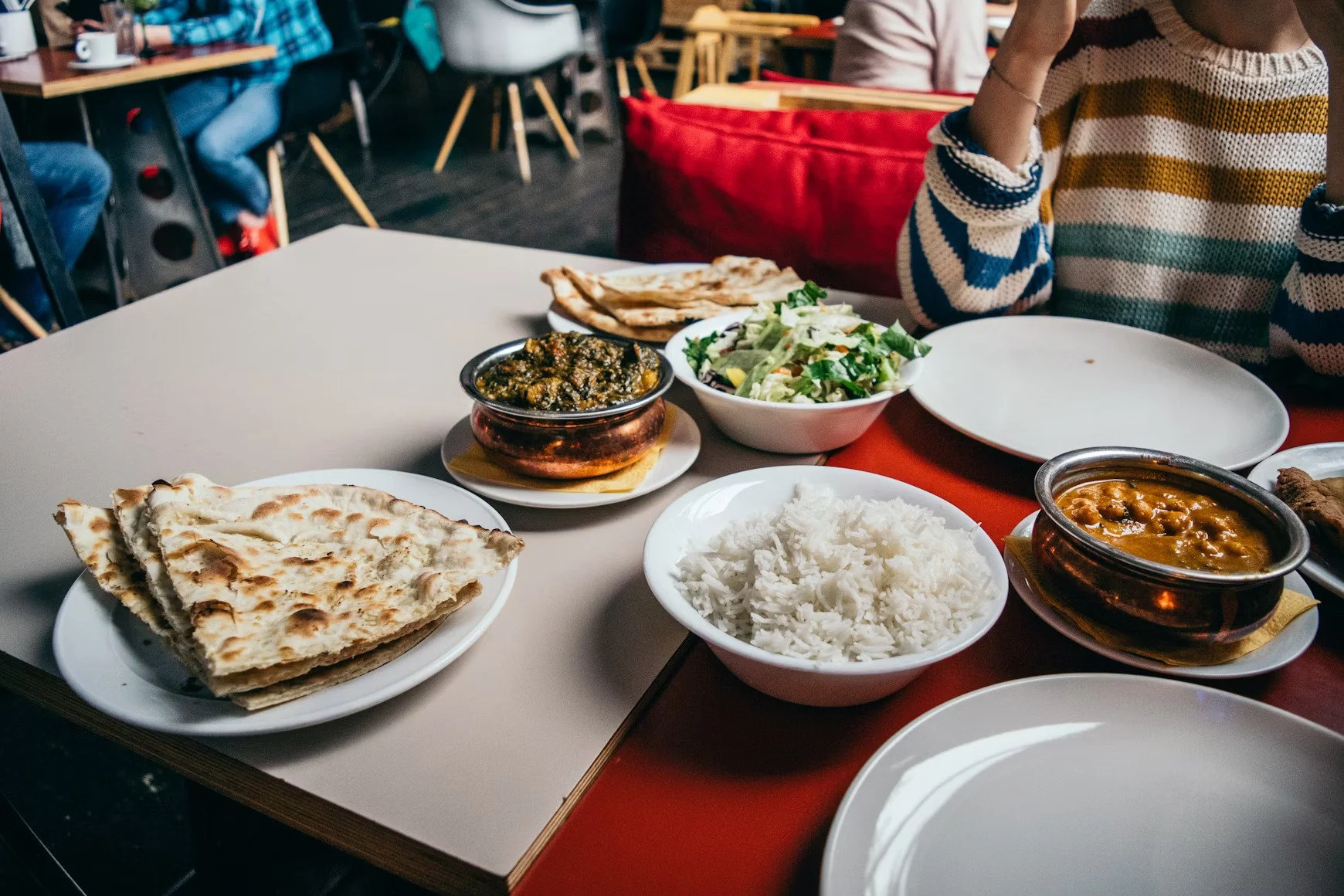 Table of Indian food including naan bread, a bowl of spinach curry, a bowl of rice, a salad, and a bowl of chickpea curry.