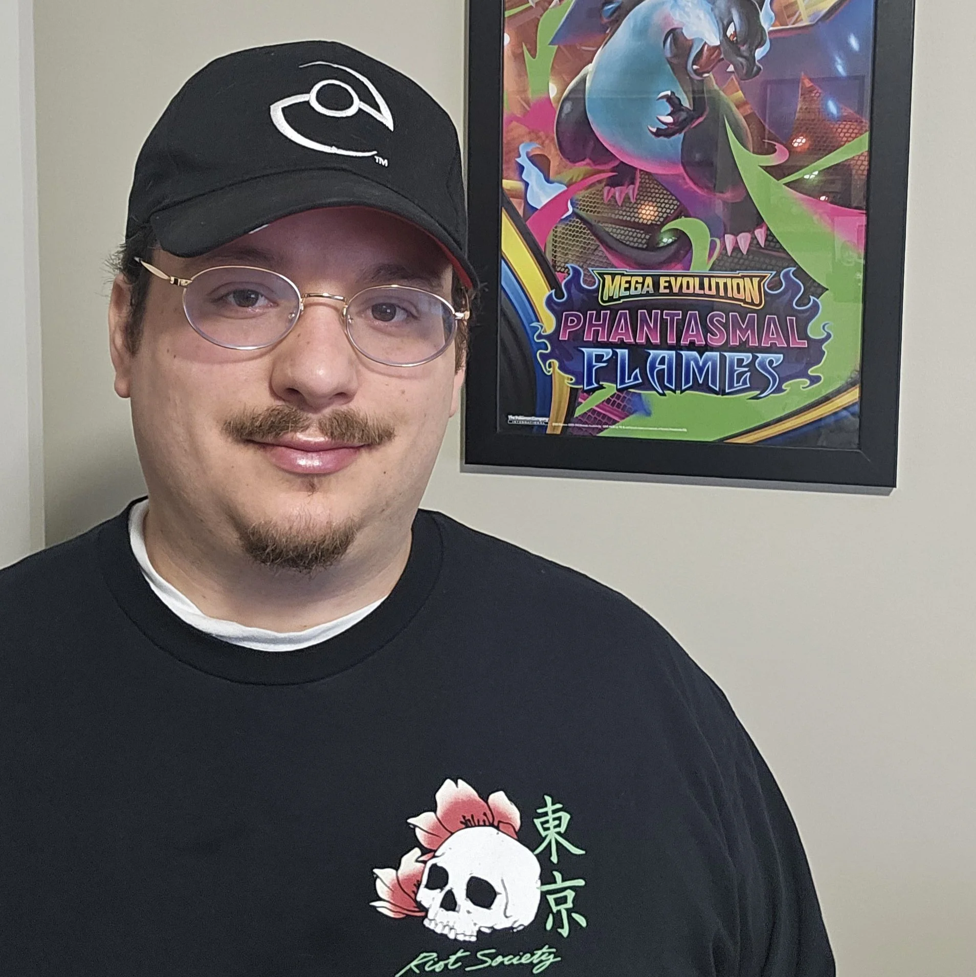 A photo of Marco D'Alelio the managing editor for Devon Corp. Behind him is a framed poster of the Pokemon Mega Charizard X with the words Mega Evolution Phantasmal Flames.