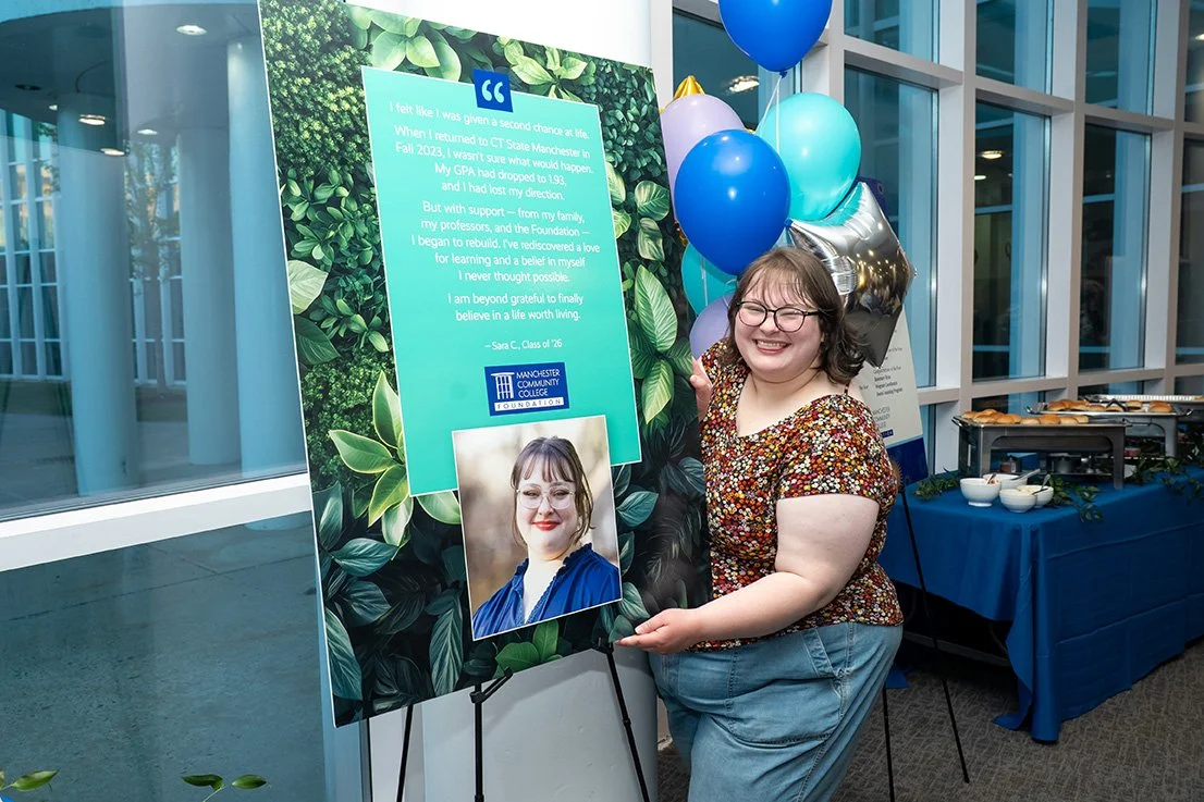 Student intern Sara smiling beside a poster featuring her CT State Manchester Foundation story at the donor and volunteer recognition event.