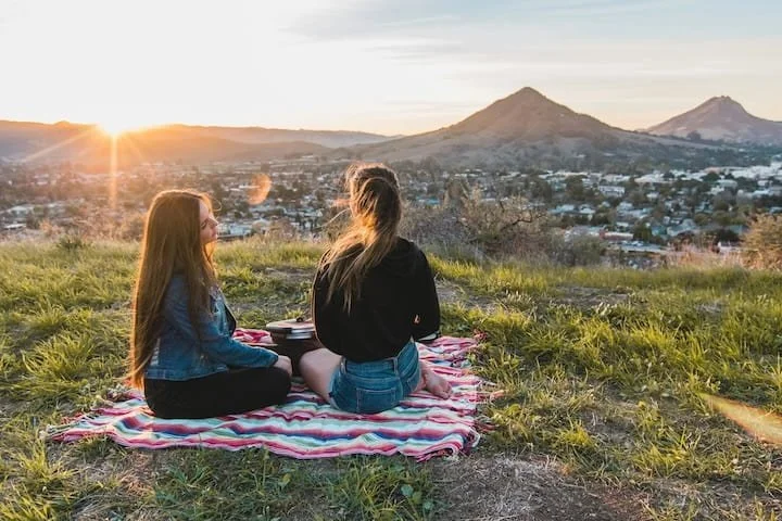 two college students sitting on a blanket watching the sunset