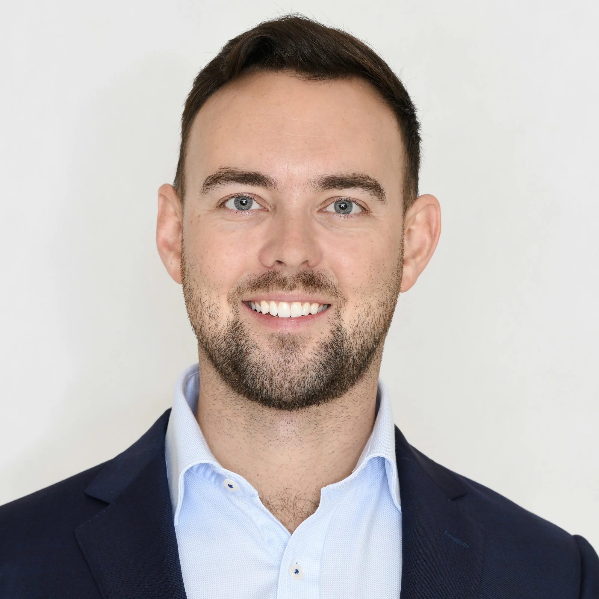 Smiling man in a suit, headshot against a light background.