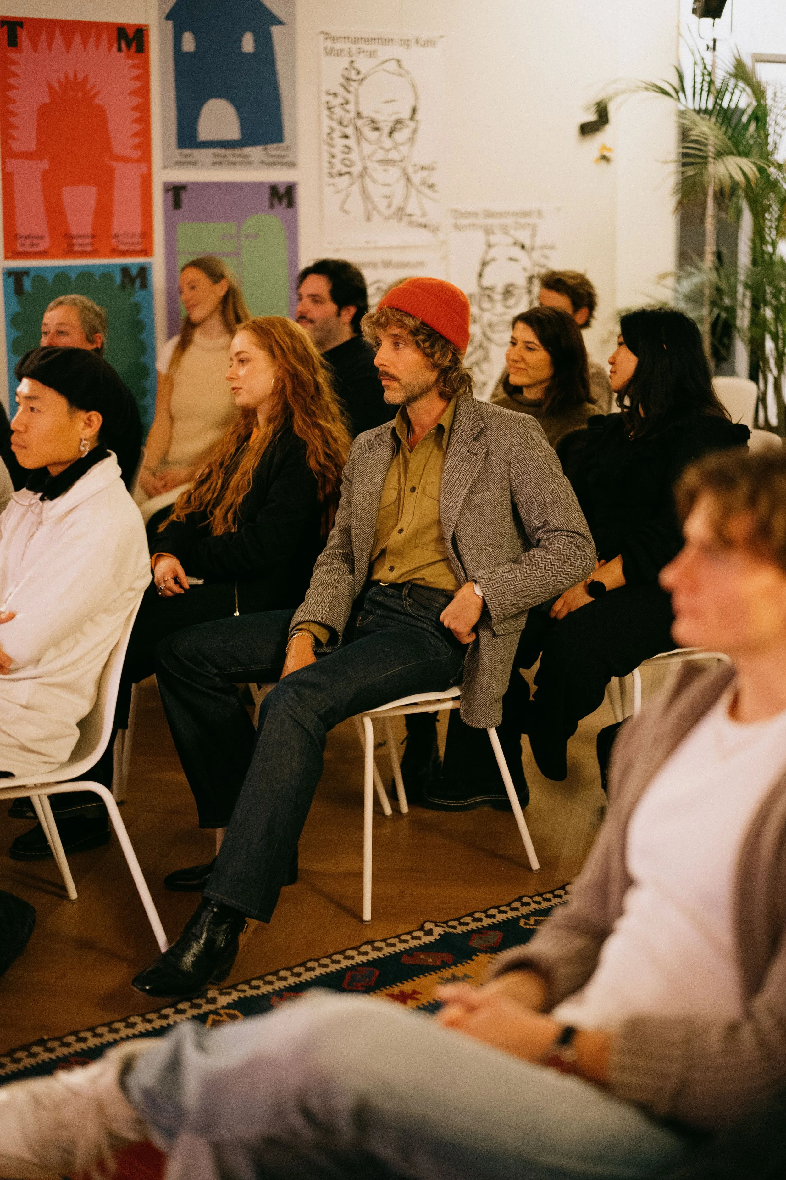 People attending a presentation or event in a room decorated with colorful posters and black-and-white sketches on the wall.