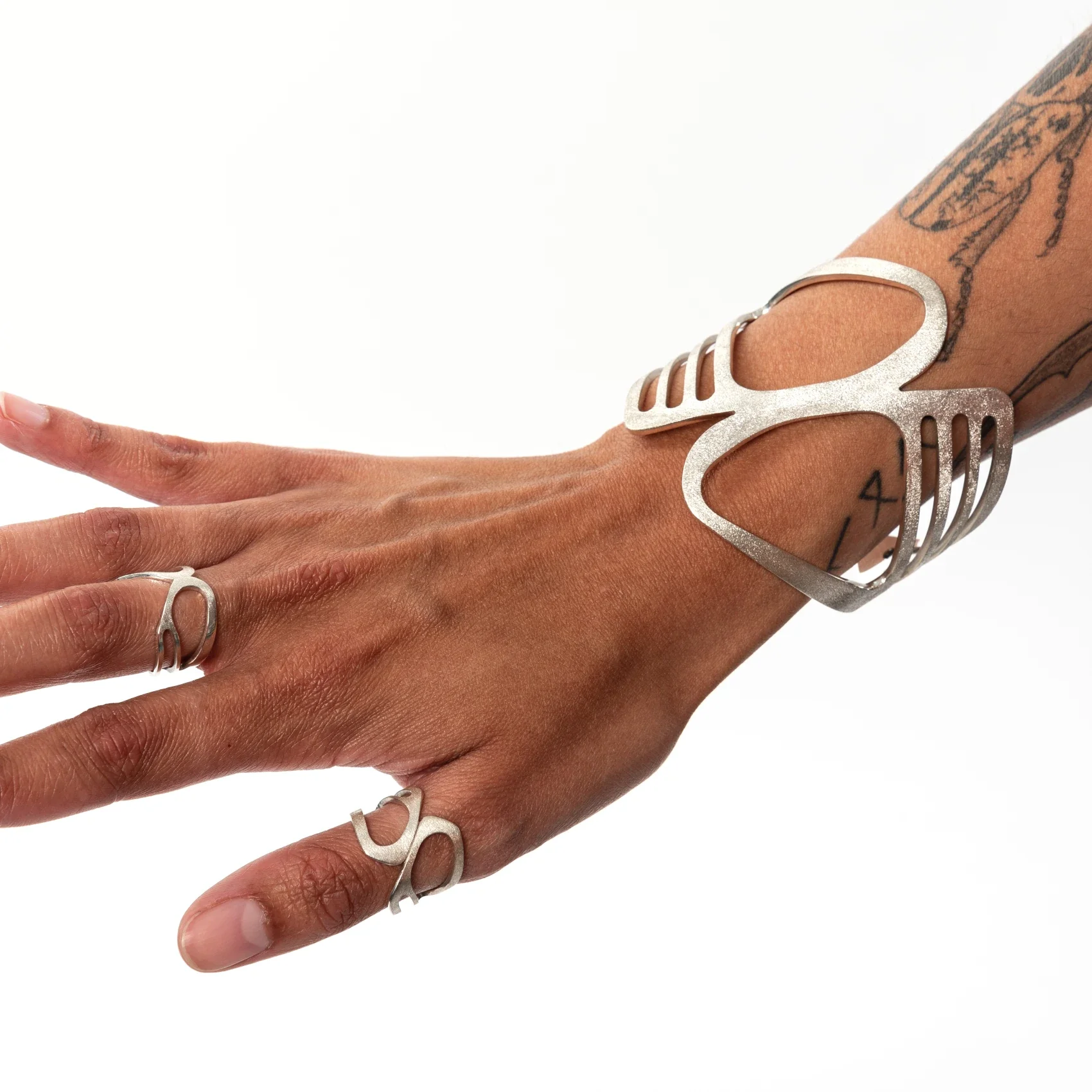 Close-up of a hand wearing Roxwoods jewellery, including sterling silver rings and a wide silver cuff bracelet, on a white background.