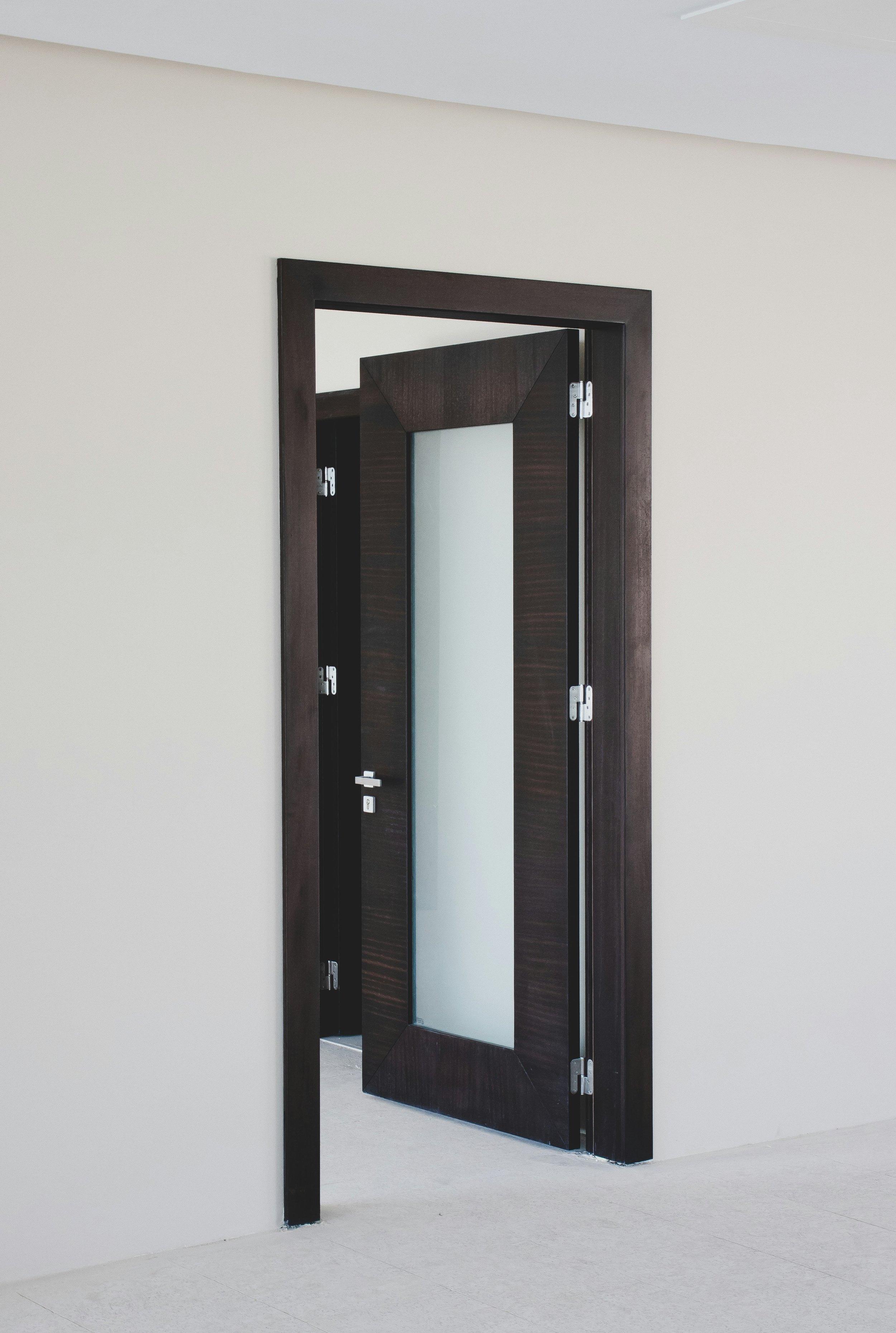 Porta aperta con cornice di legno scuro, parzialmente aperta, in una parete bianca interamente liscia.