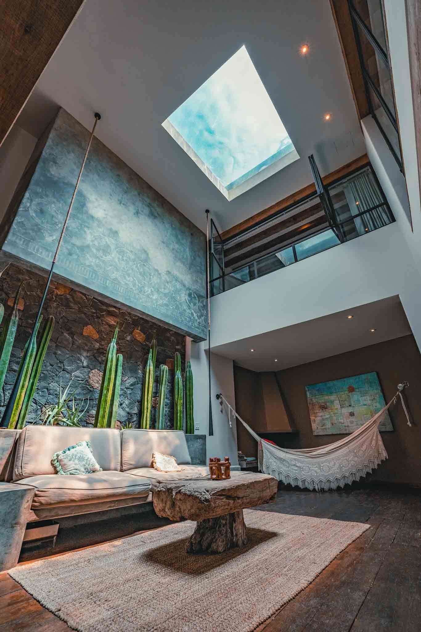 Living room with a hammock, stone and wood accents, a beige sofa with pillows, a rustic coffee table, and a skylight ceiling