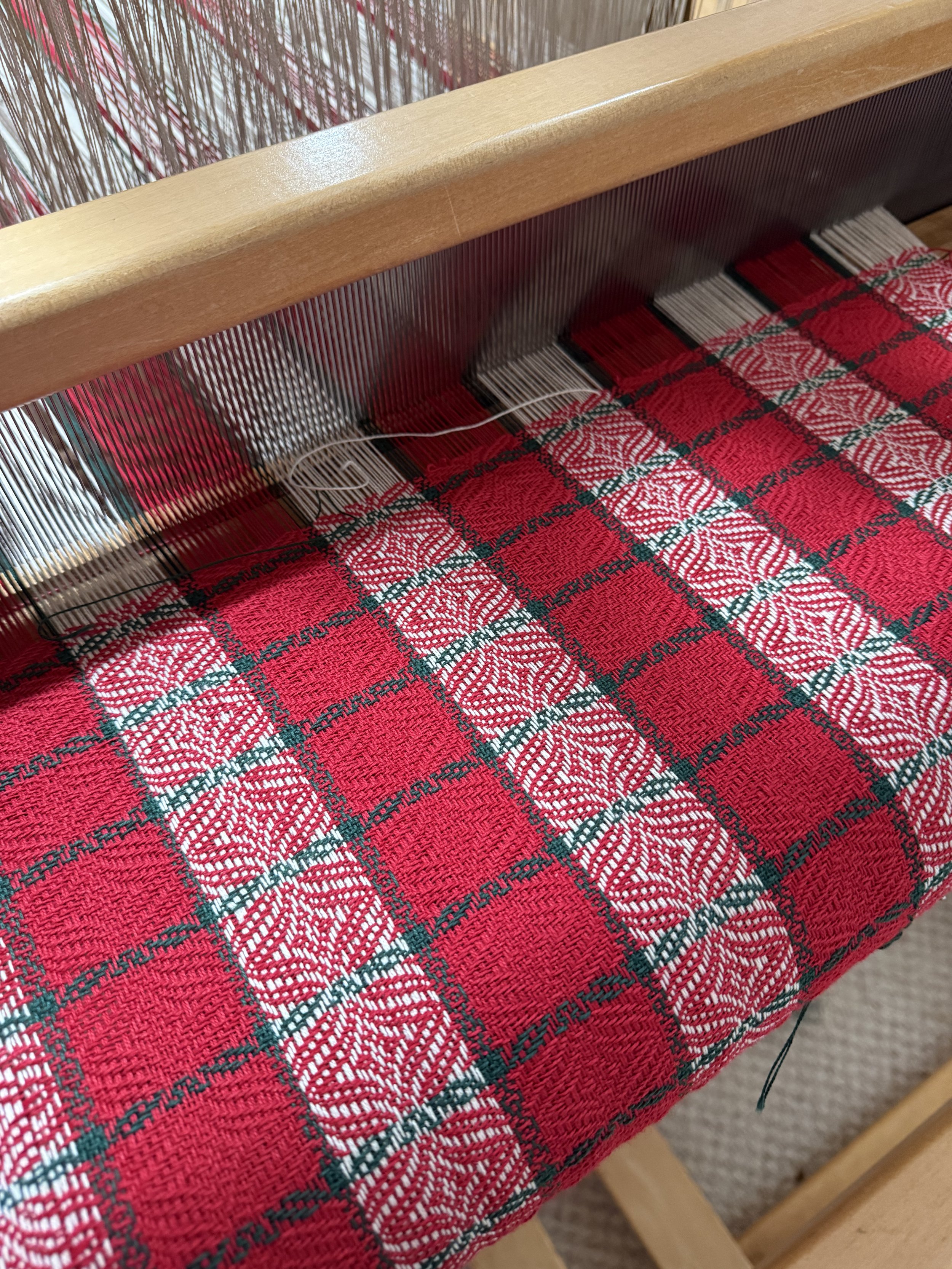 Close-up view of a weaving loom with red, green, and white plaid fabric being woven.