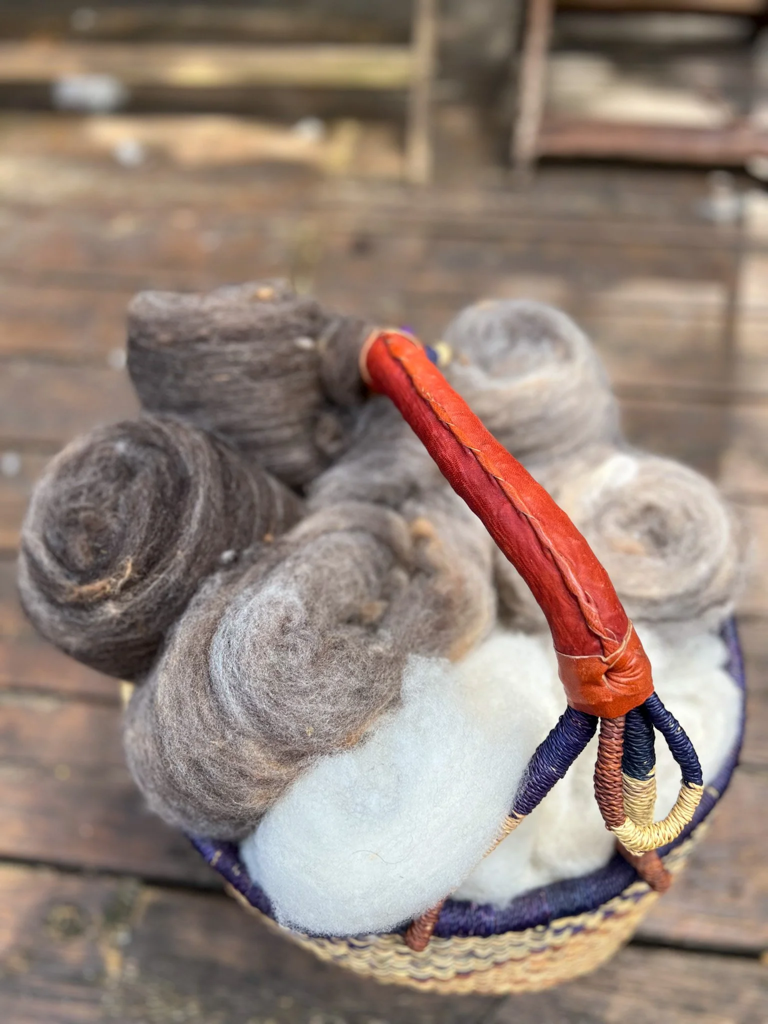 Close-up of a basket of wool batts, with a blurred background of a wooden surface.