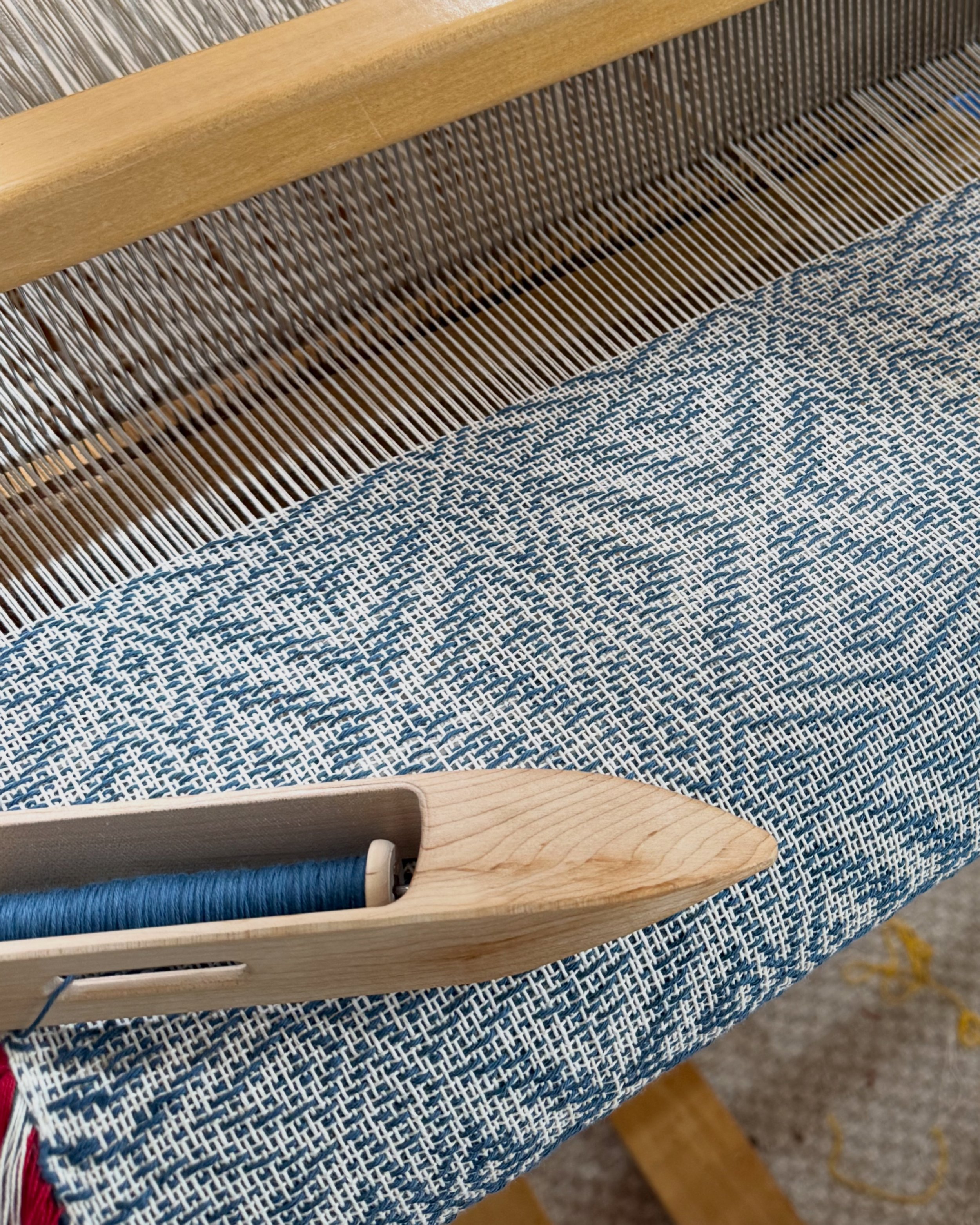 Close-up of a weaving loom with partially woven blue and white fabric, wooden parts, and a blue yarn.