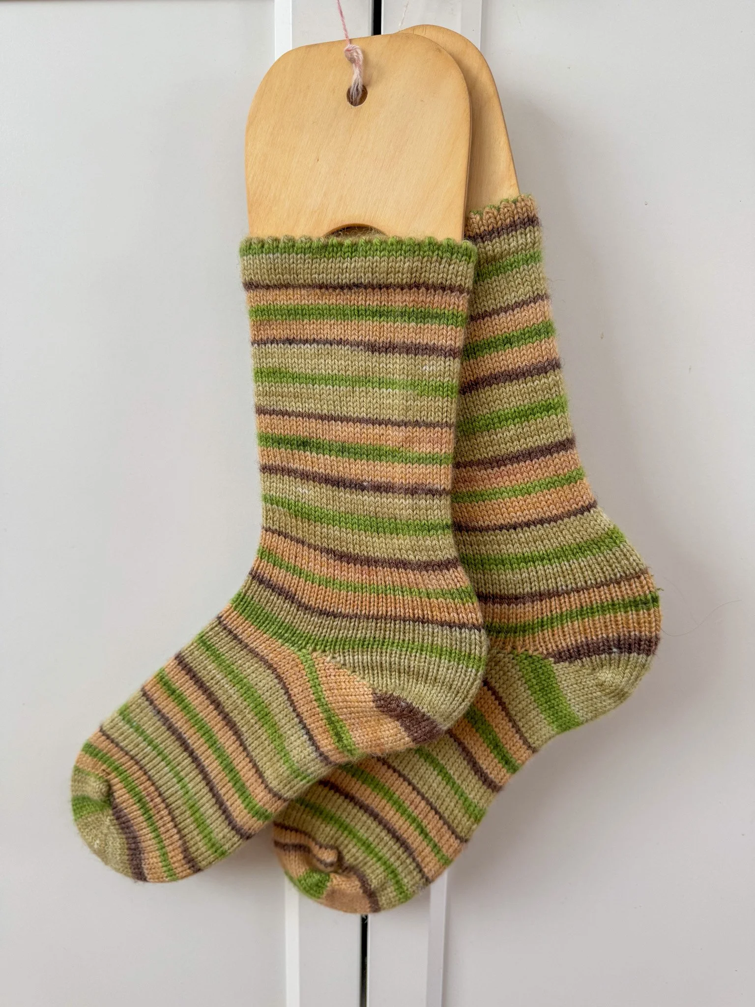 A pair of multicolored striped knit socks hanging on a wooden hanger against a white background.