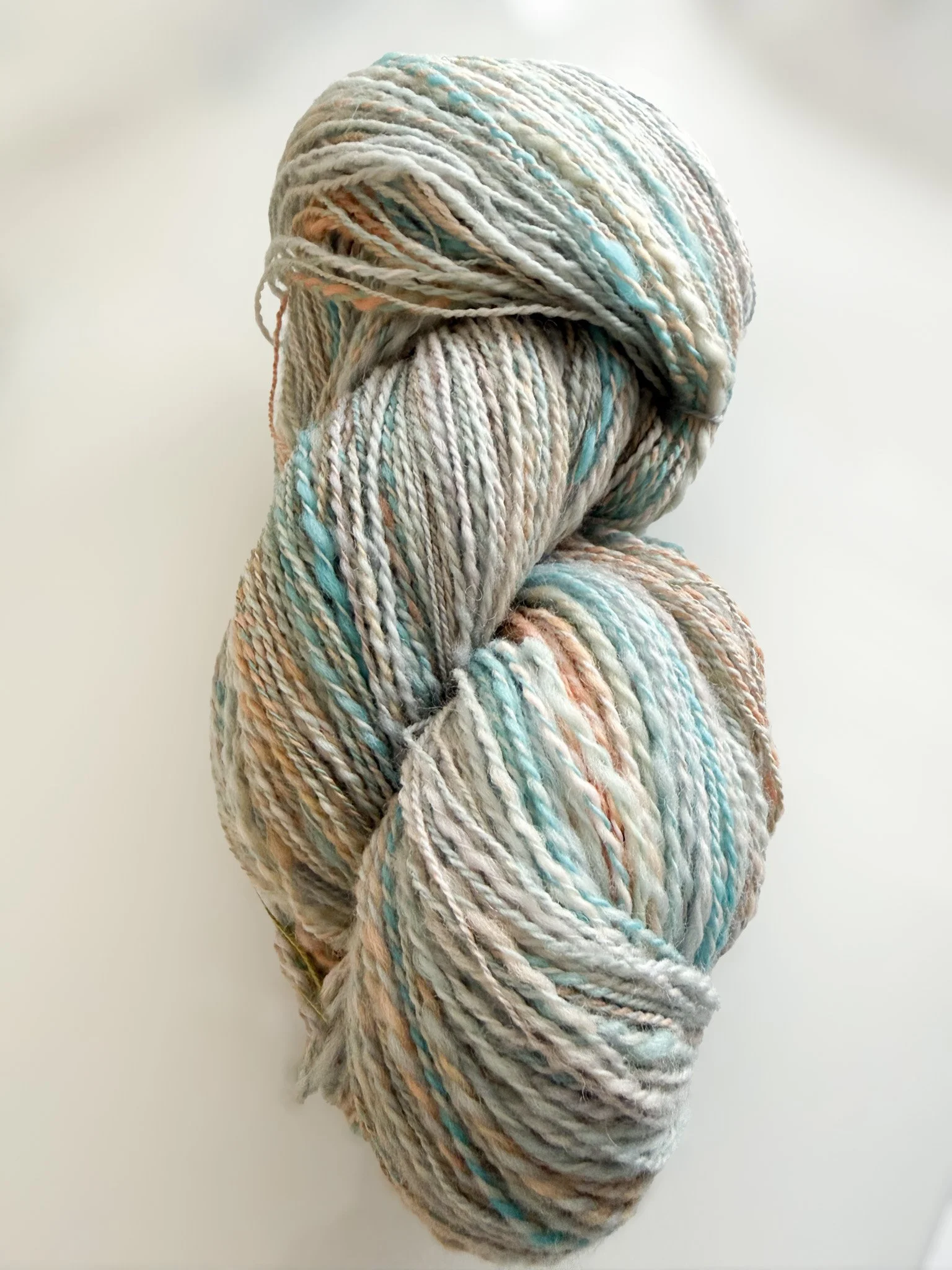 A skein of multicolored yarn with shades of white, blue, orange, and brown, resting against a white background.