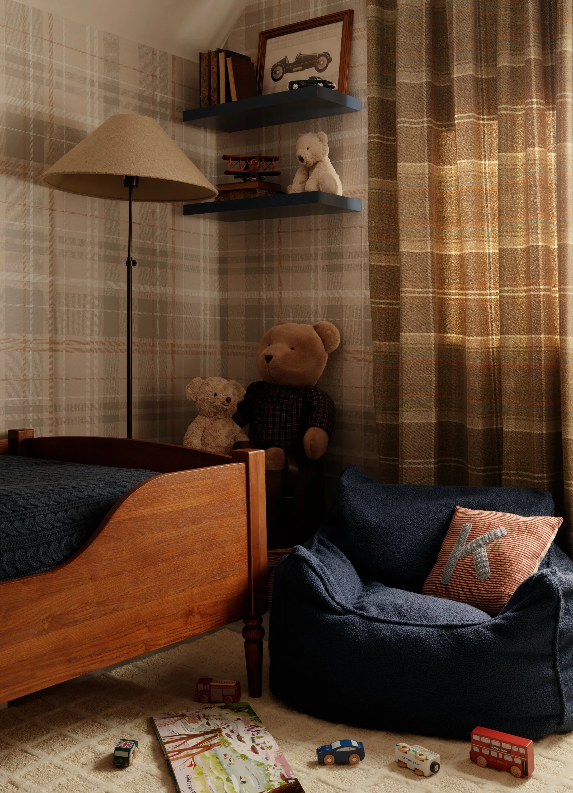 Cosy reading corner with navy chair and heritage plaid wallpaper in boy’s bedroom.