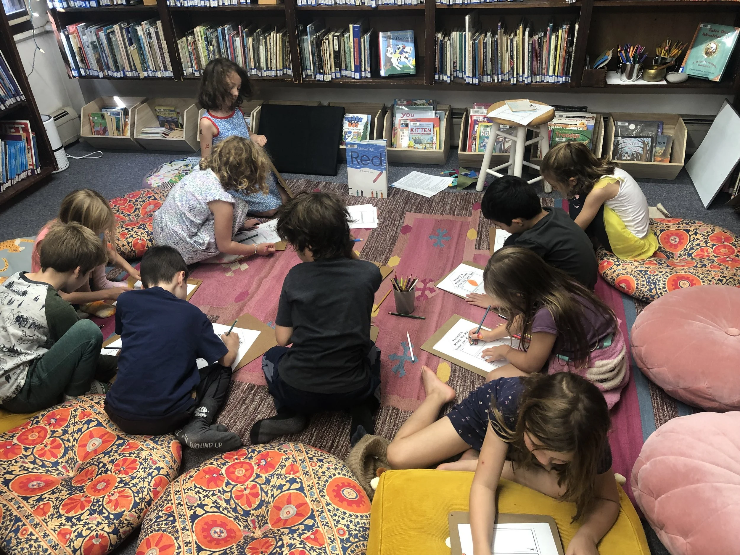eight children with drawing on clip boards on the floor in the library