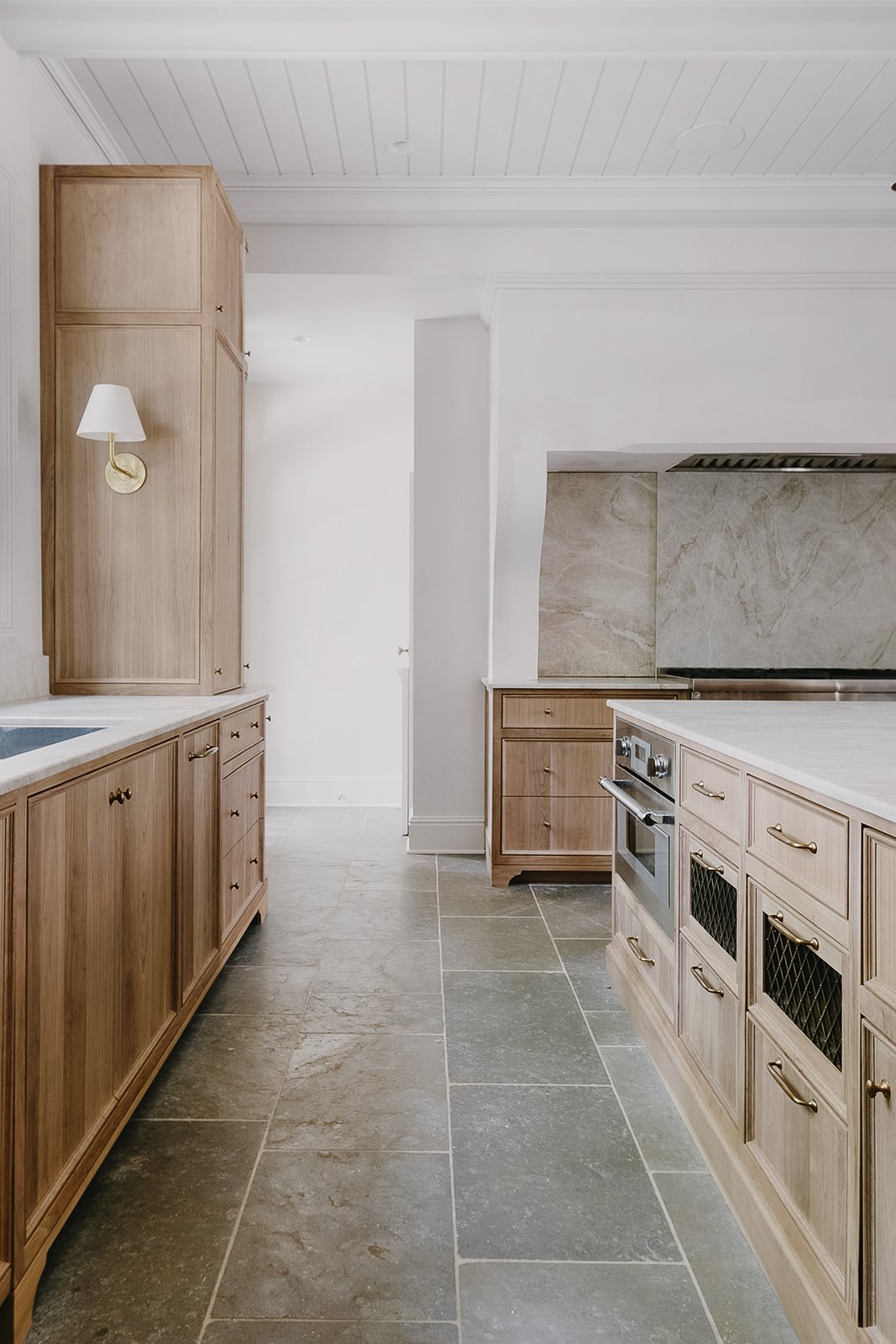 A timeless kitchen with light wood cabinets, gray tiled flooring, and a marble backsplash.