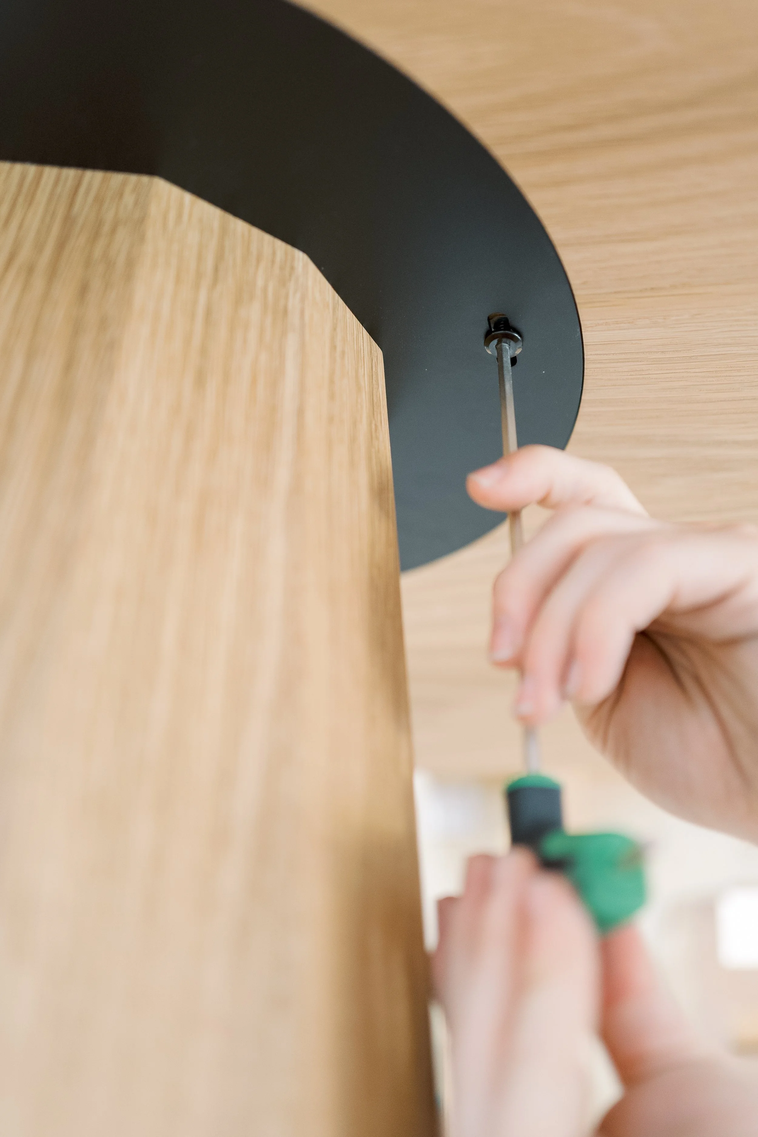 Person using a allen key to assemble or secure a piece of furniture with a wooden surface and a black circular support.