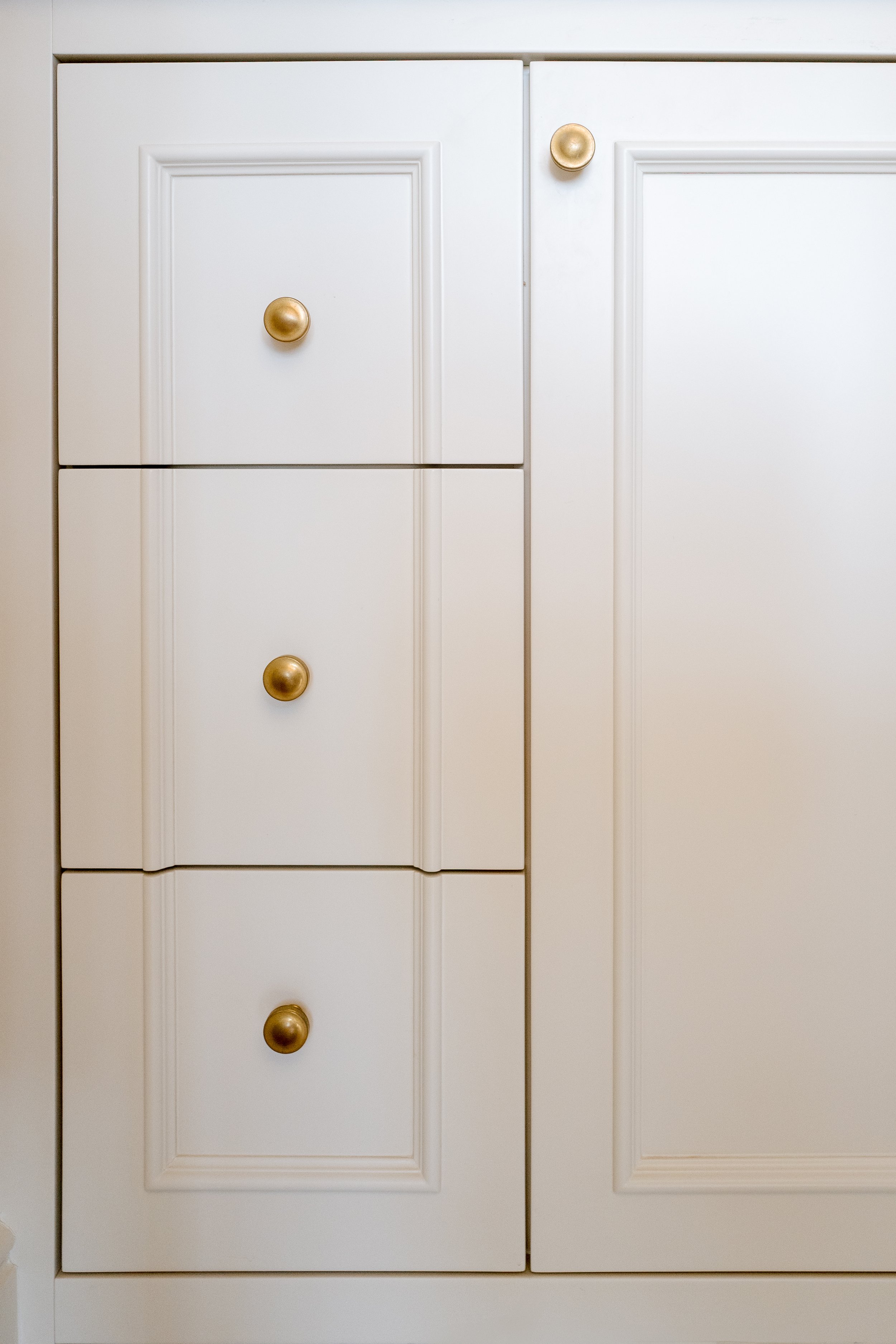 Close-up of white kitchen cabinets with gold knobs.