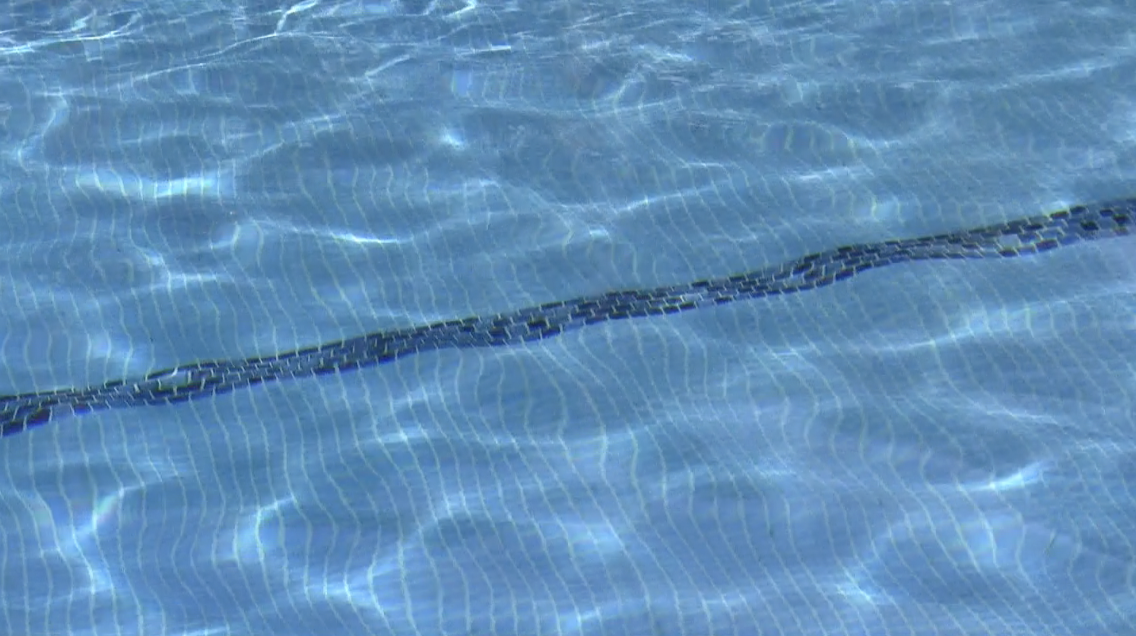 Close-up of a swimming pool's tiled water surface, showing light reflections and a dark line of tiles.