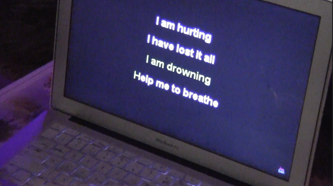 A laptop screen displaying the text "I am hurting, I have lost it all, I am drowning, Help me to breathe" in white and green against a dark background.