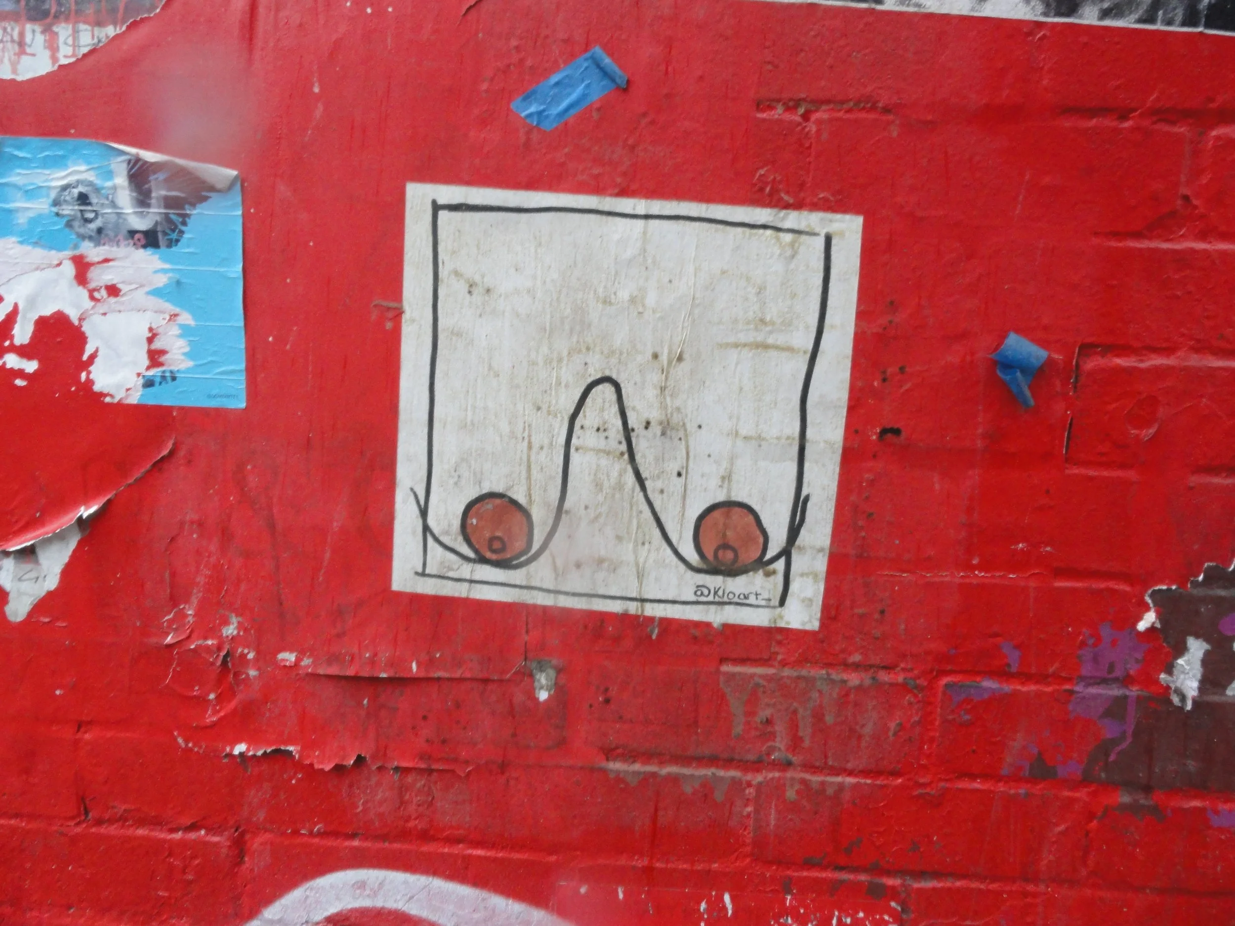 A hand-drawn diagram of a soccer field, showing two goals, with black lines and orange circles inside the goals. The drawing is on a white paper pinned to a red brick wall, with small patches of torn posters and blue tape nearby.