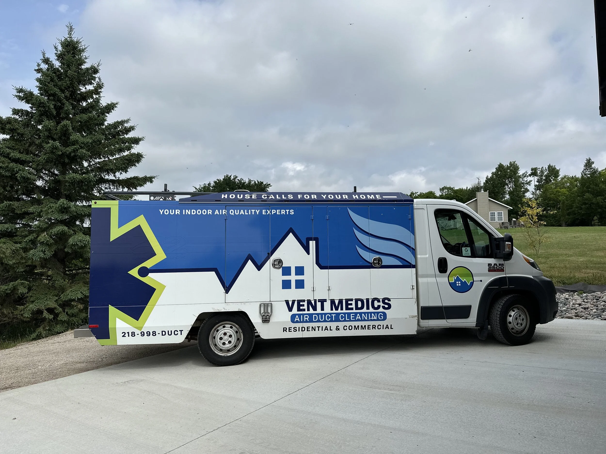 Service van for Vent Medics, an indoor air quality and duct cleaning company, parked on a driveway next to a grassy yard with a house and trees in the background.