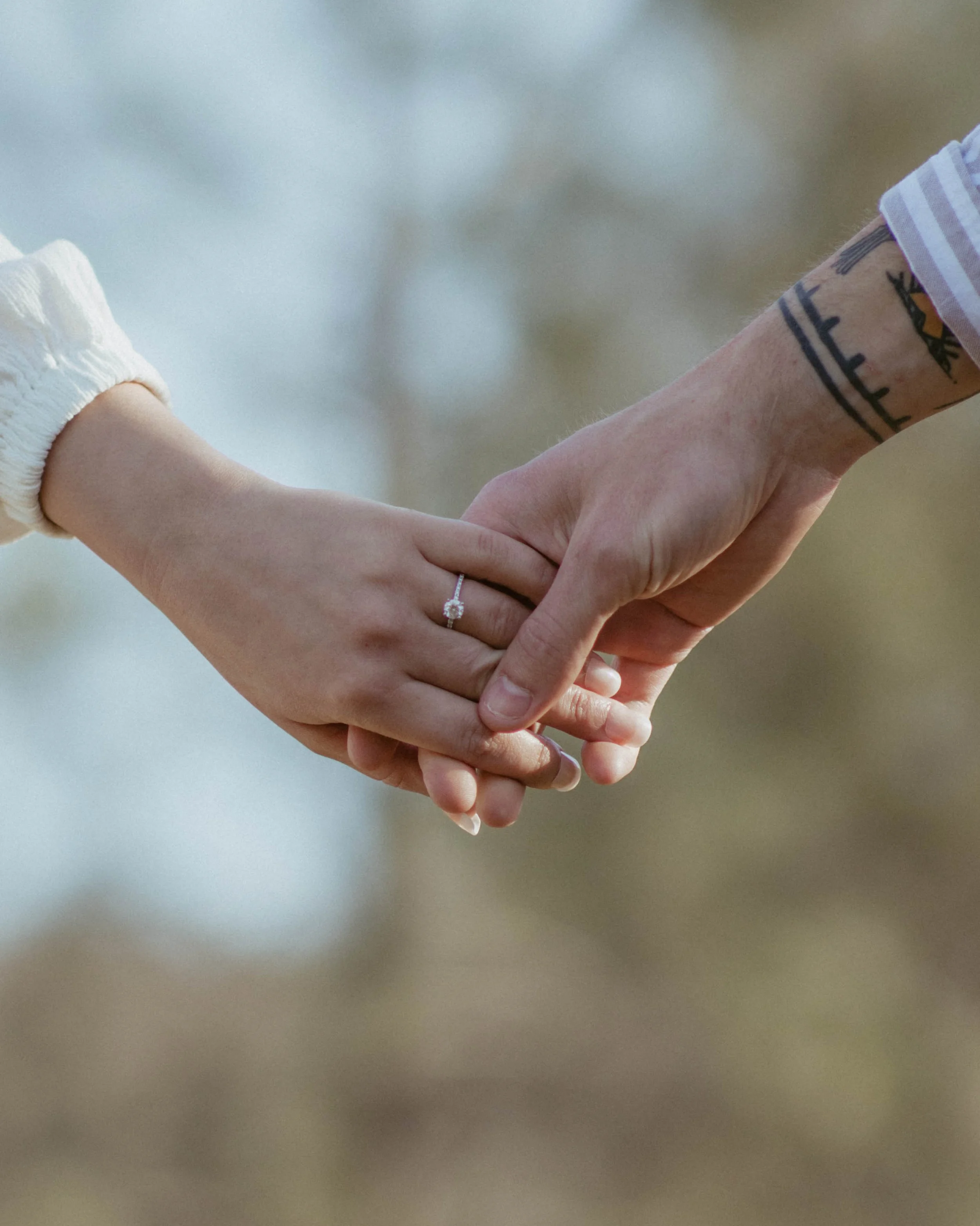 Woman wearing engagement ring holding man's hand with tattoos on his wrist