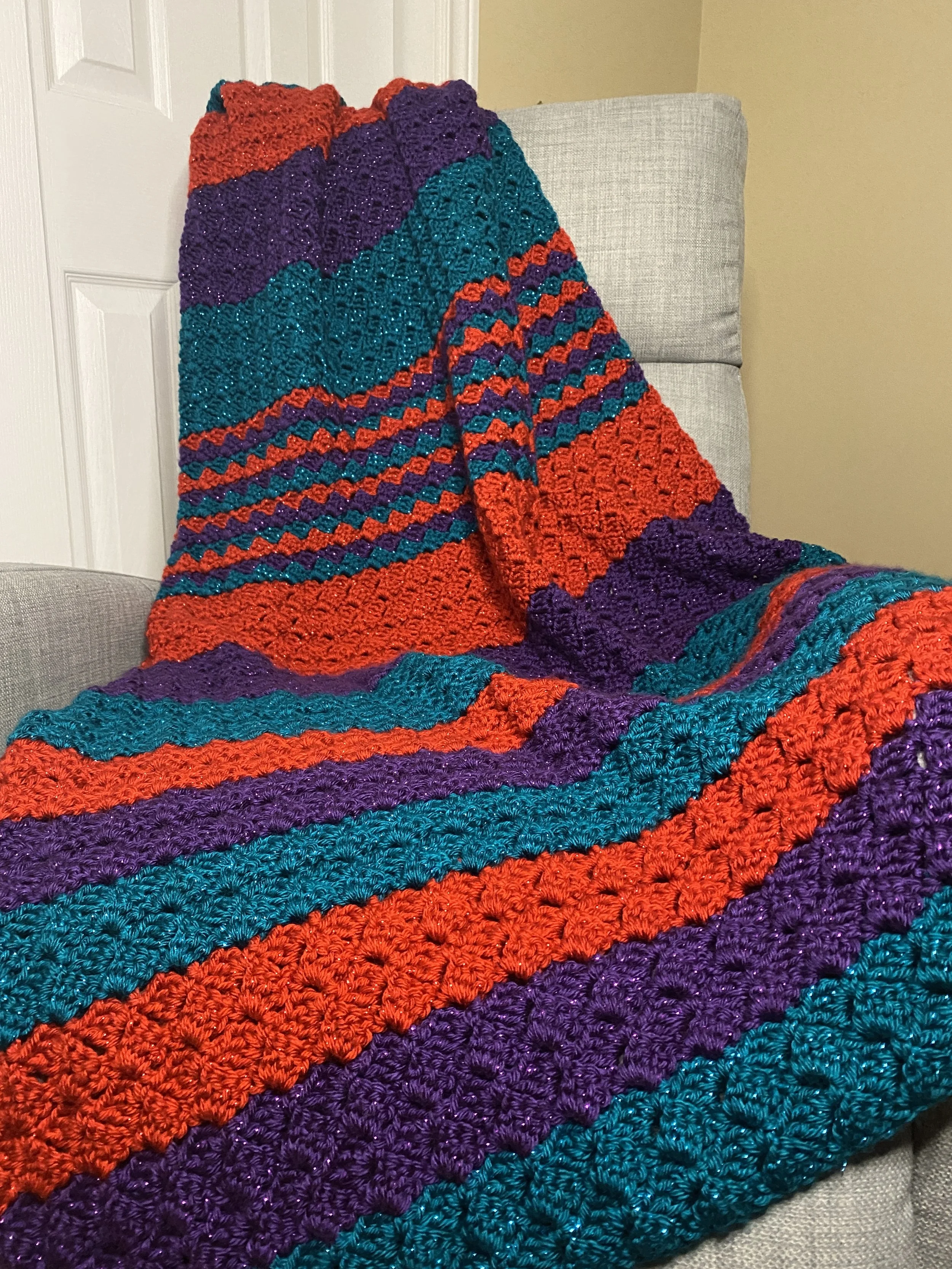 Colorful, crocheted blanket with red, purple, turquoise, and blue stripes, draped over a light gray sofa.