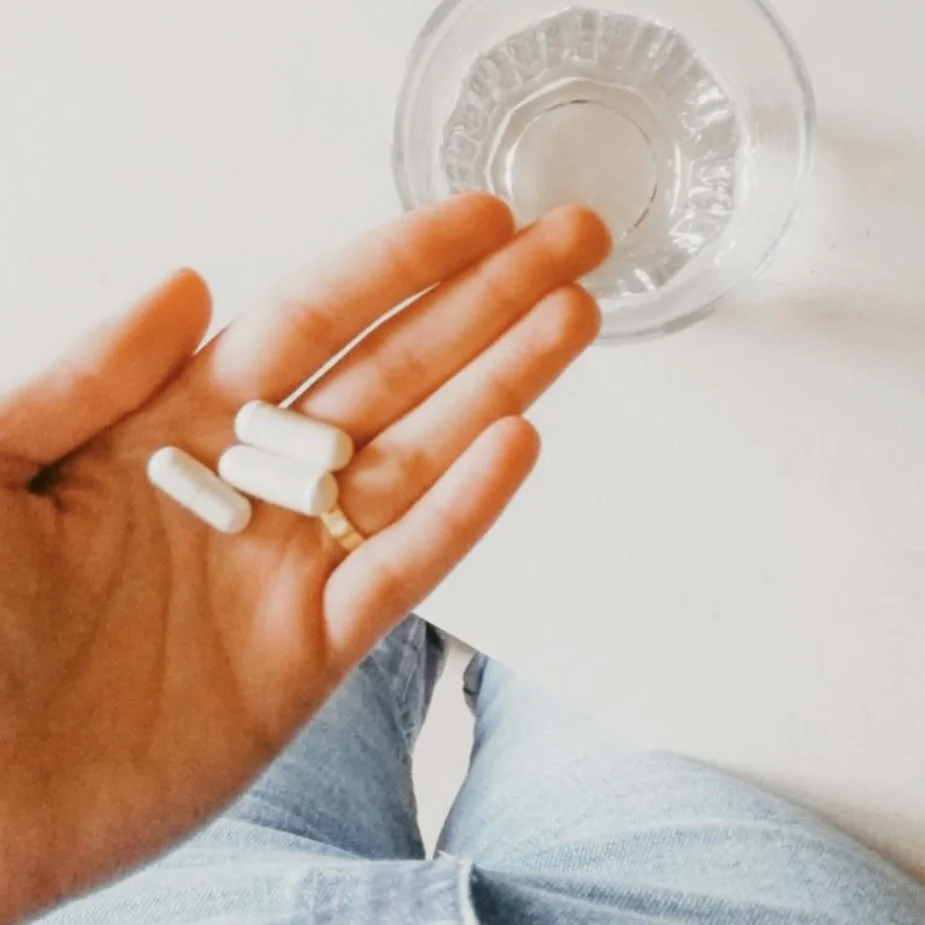 supplements held in hand with glass of water on the table