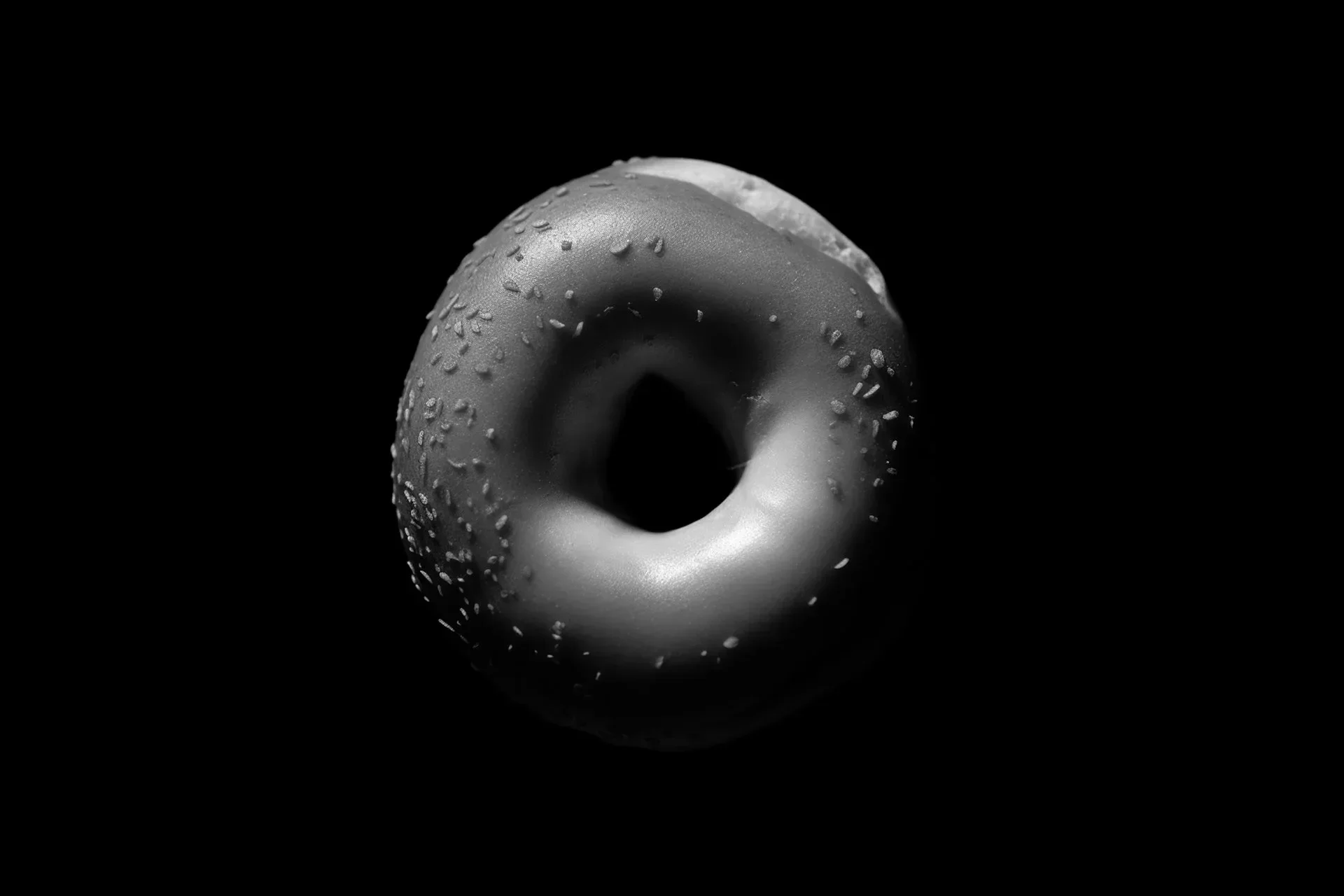 Black and white close-up of a doughnut with sprinkles on a dark background.