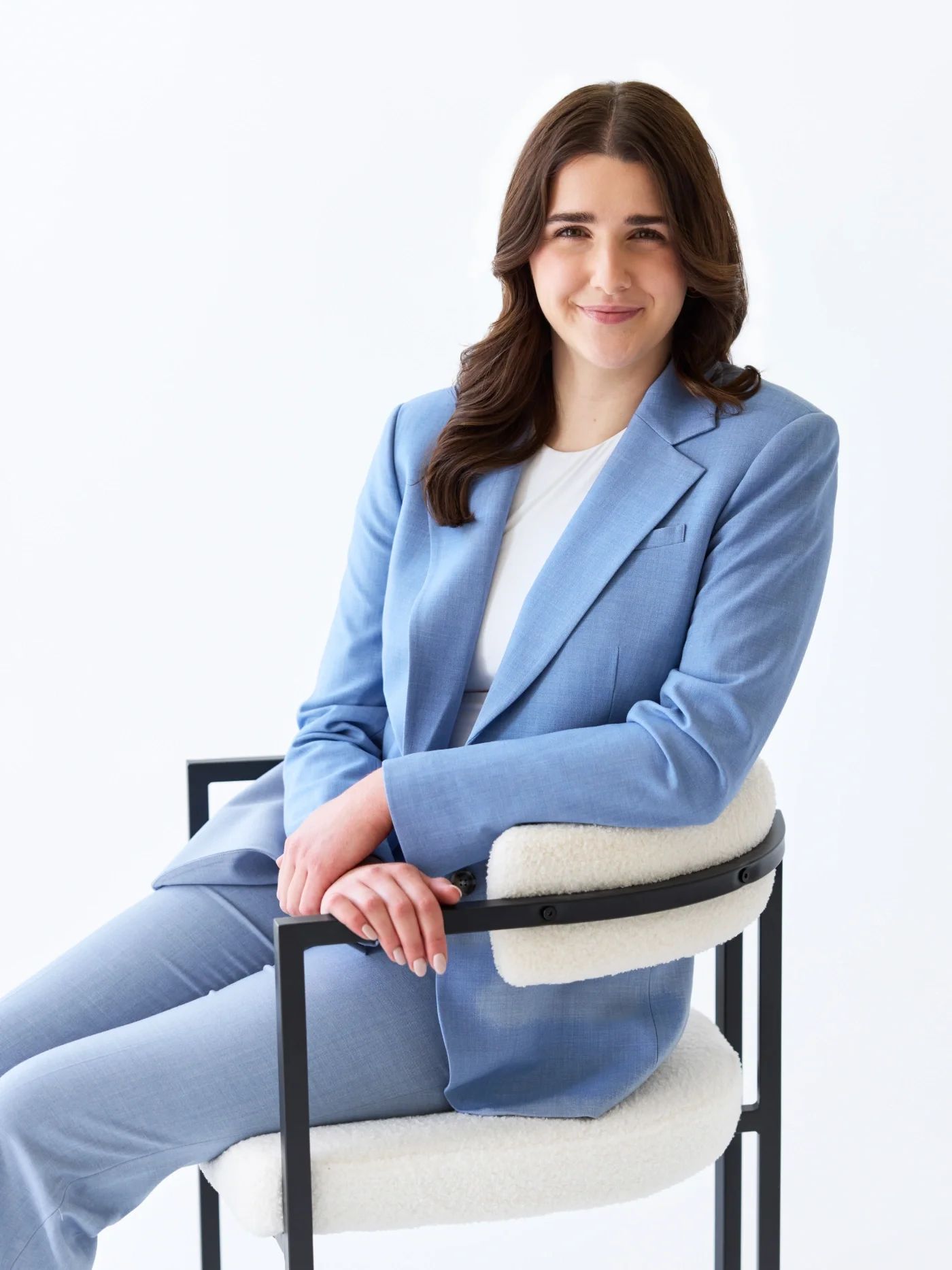 Taylor of With Ease Therapy Space in Guelph wearing a light blue suit, sitting on a chair, and smiling at the camera.