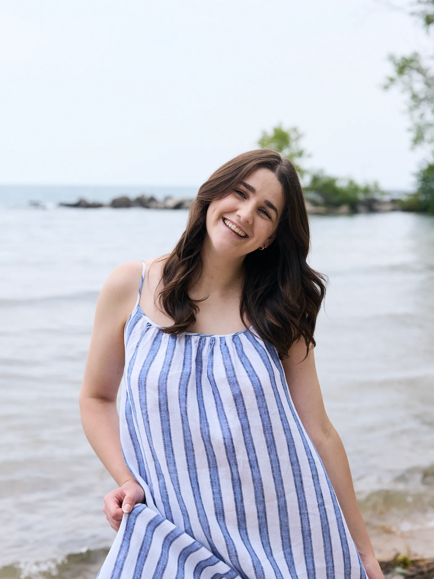 Taylor of With Ease Therapy Space in Guelph posed in front of a lake, smiling at the camera, wearing a white and blue flowy dress.