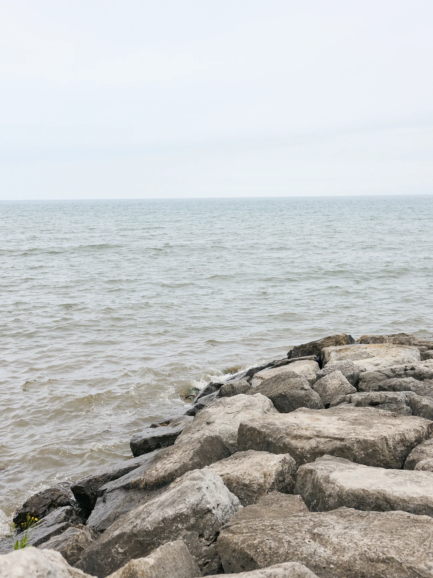 A rocky shoreline with large stones in the foreground of a lake.