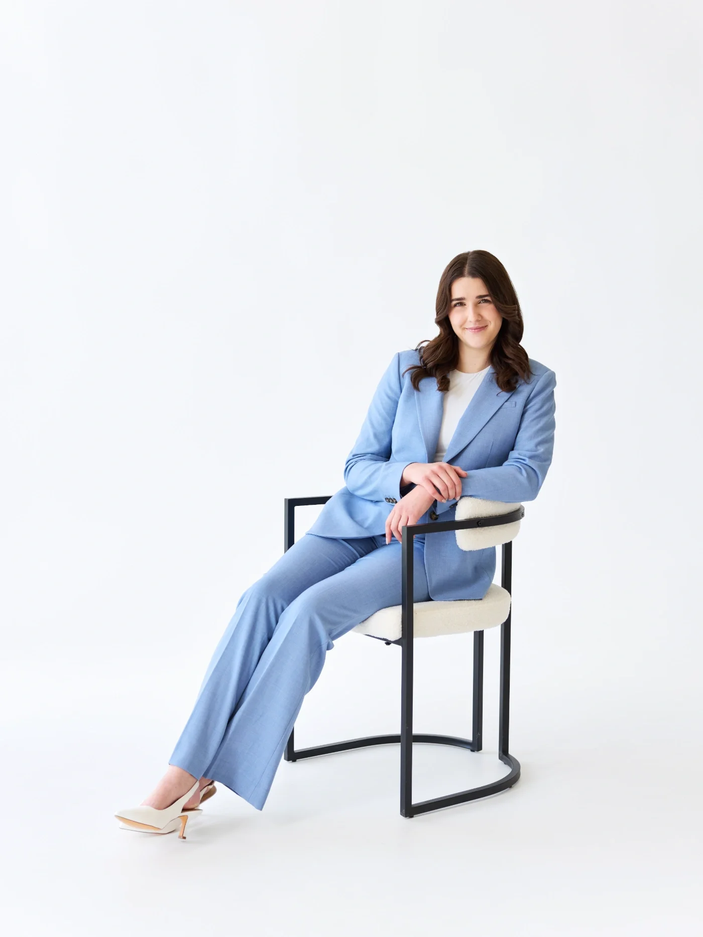 Taylor of With Ease Therapy Space in Guelph wearing a light blue suit, sitting on a chair, and smiling at the camera.