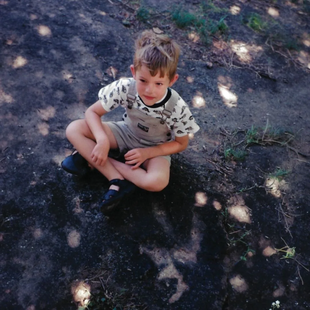 Young Jeremy sitting in dirt next to dinosaur tracks