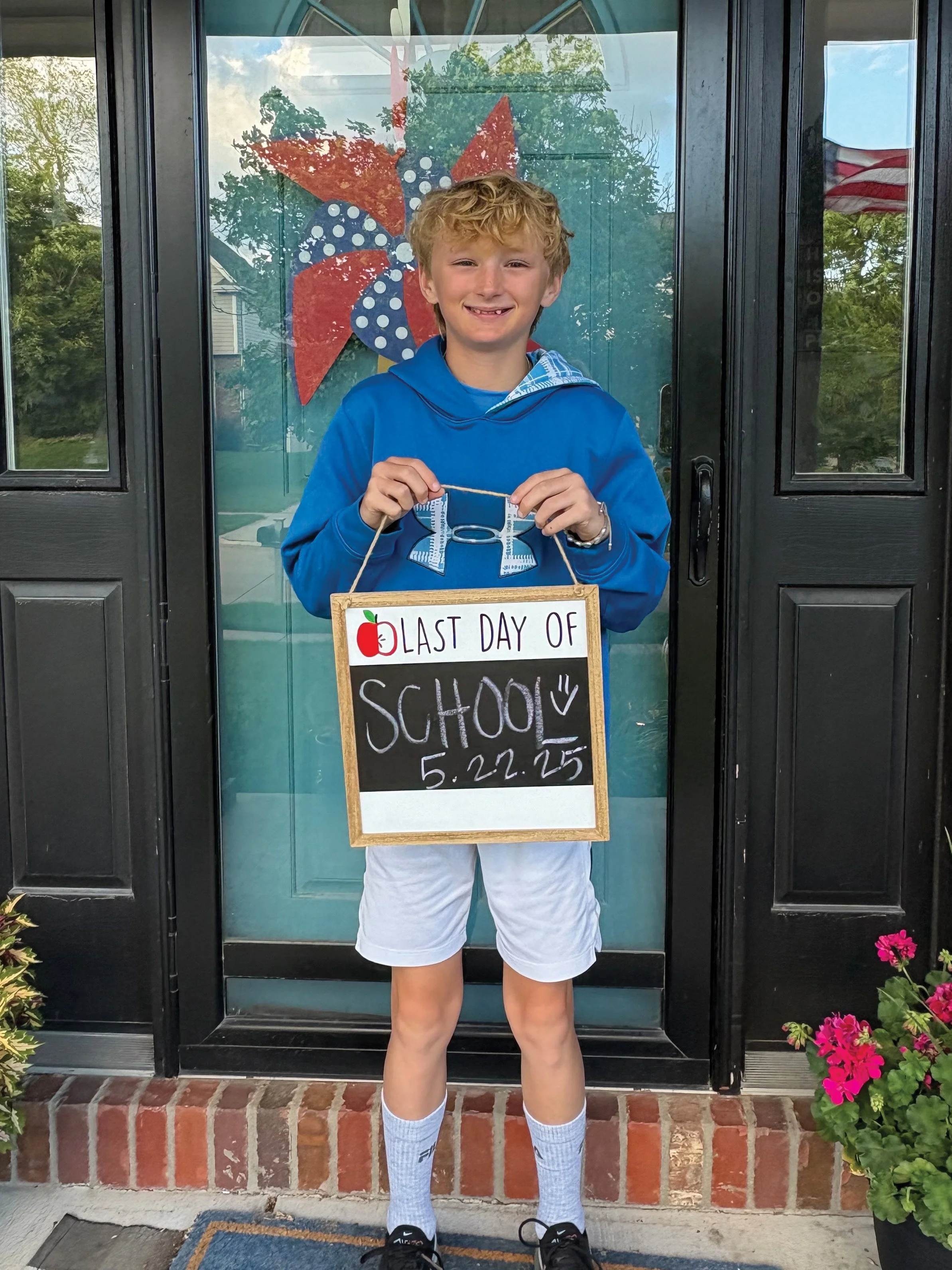 Hudson standing infront of a door holding a last day of school sign