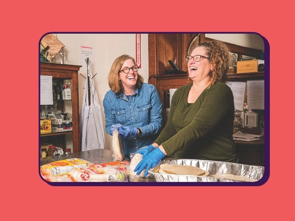 Two woman laughing in volunteer community kitchen