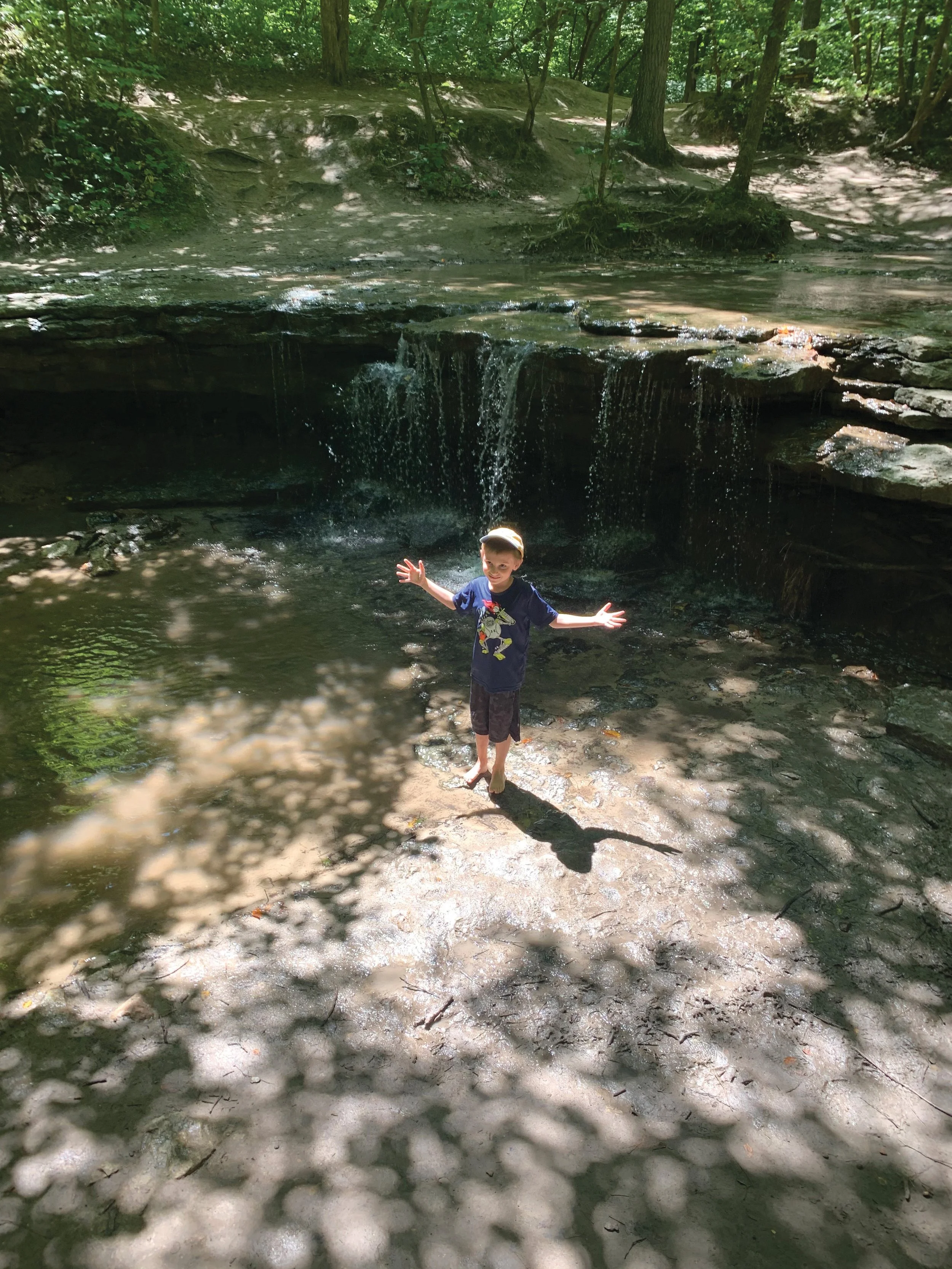 one little boy standing by a small waterfall in the woods