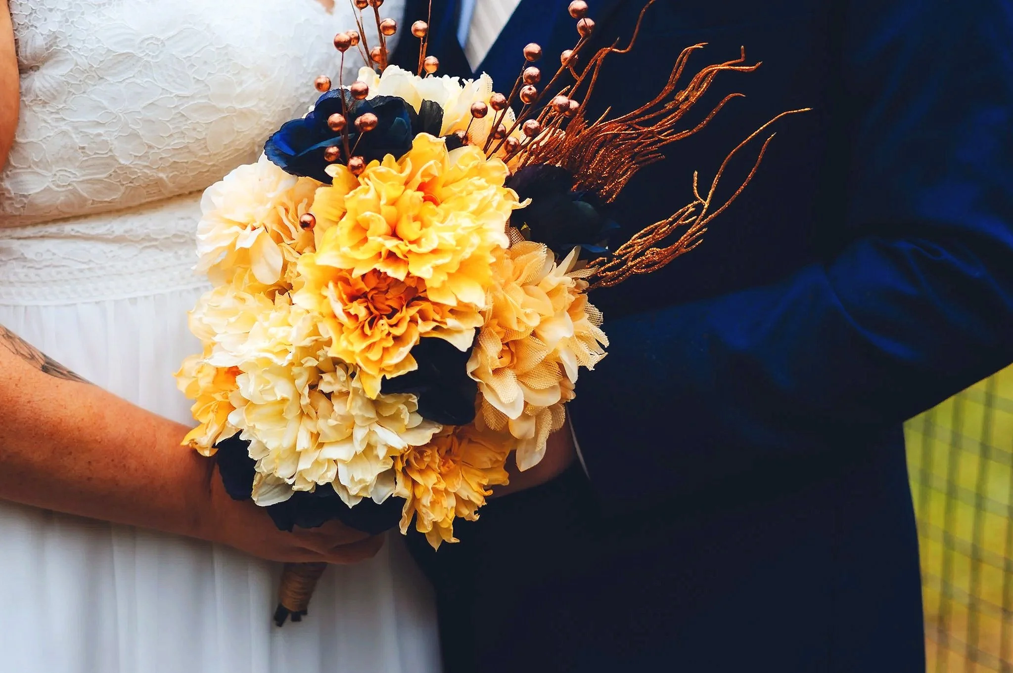 A bride and groom holding a bouquet of yellow and black flowers with brown branches during a wedding ceremony.