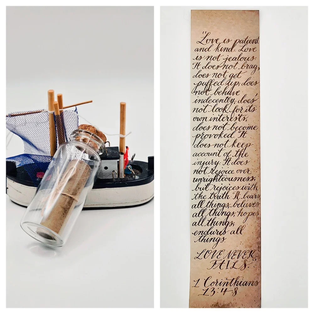 A decorative jar with a rolled paper inside is placed on a miniature model of a boat. Next to it is a vertical scroll of parchment paper with handwritten scripture quote from 1 Corinthians 13:4-8 about love.