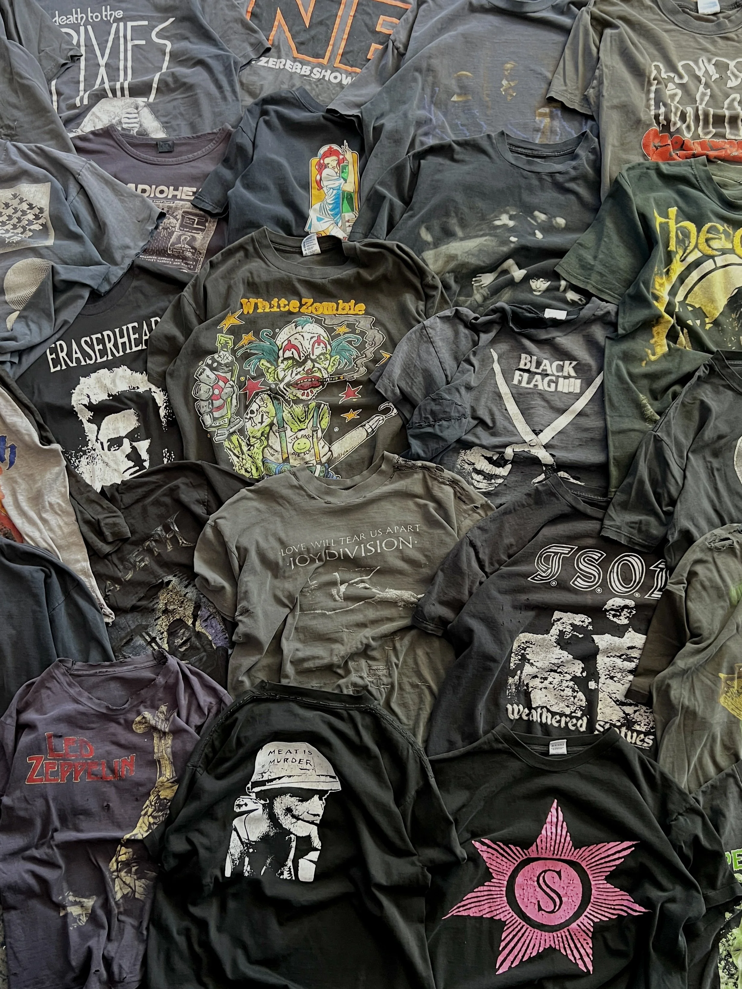 A collection of various T-shirts with band, music, and graphic designs laid out on a flat surface.