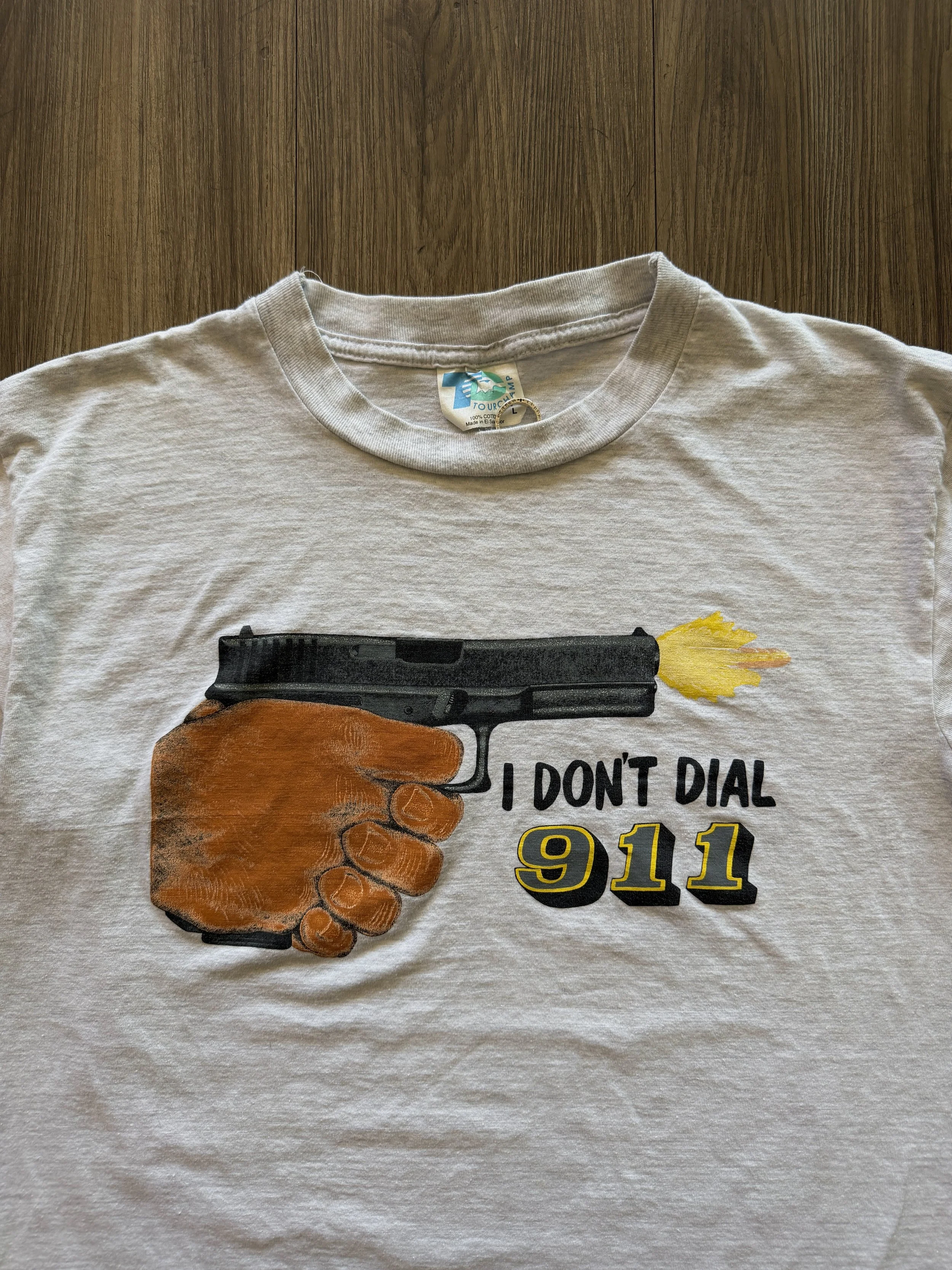 White T-shirt with a graphic of a handgun firing a yellow projectile, with text reading 'I DON'T DIAL 911'.