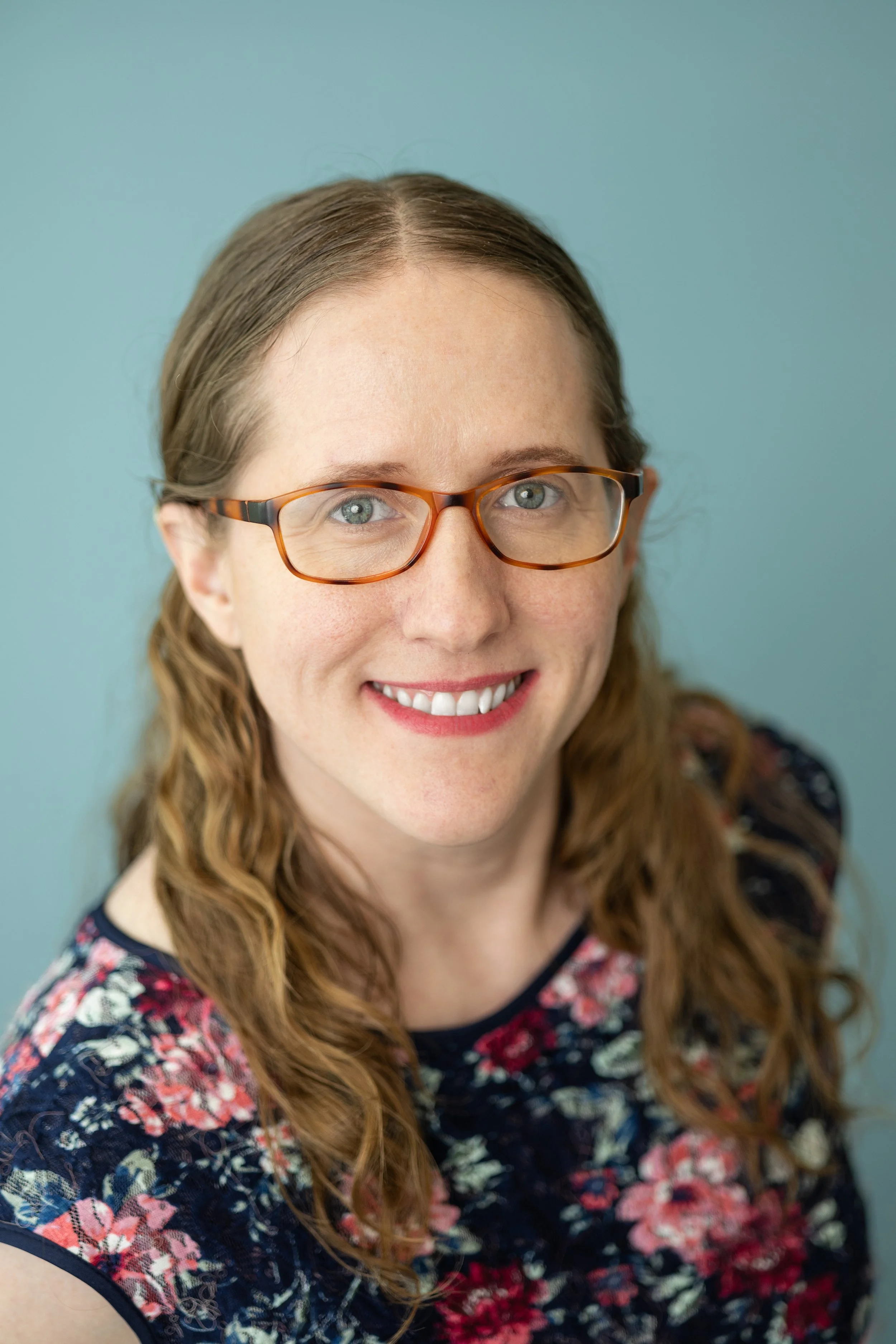Sarah Burr headshot in floral dress in front of blue background.