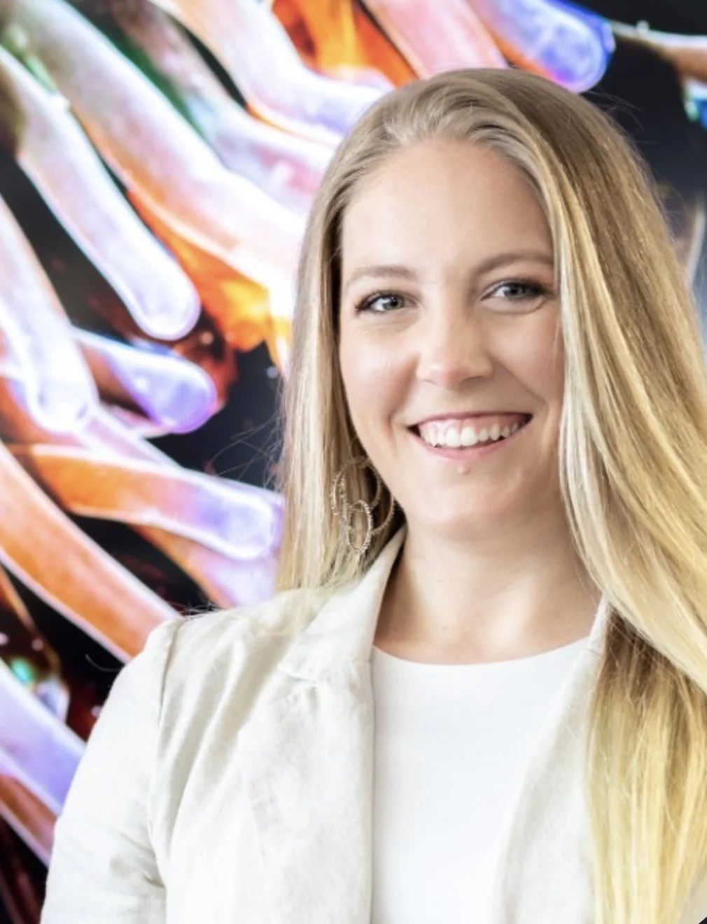 A woman with long blonde hair smiling at the camera, with colorful art of intertwined fingers in the background.