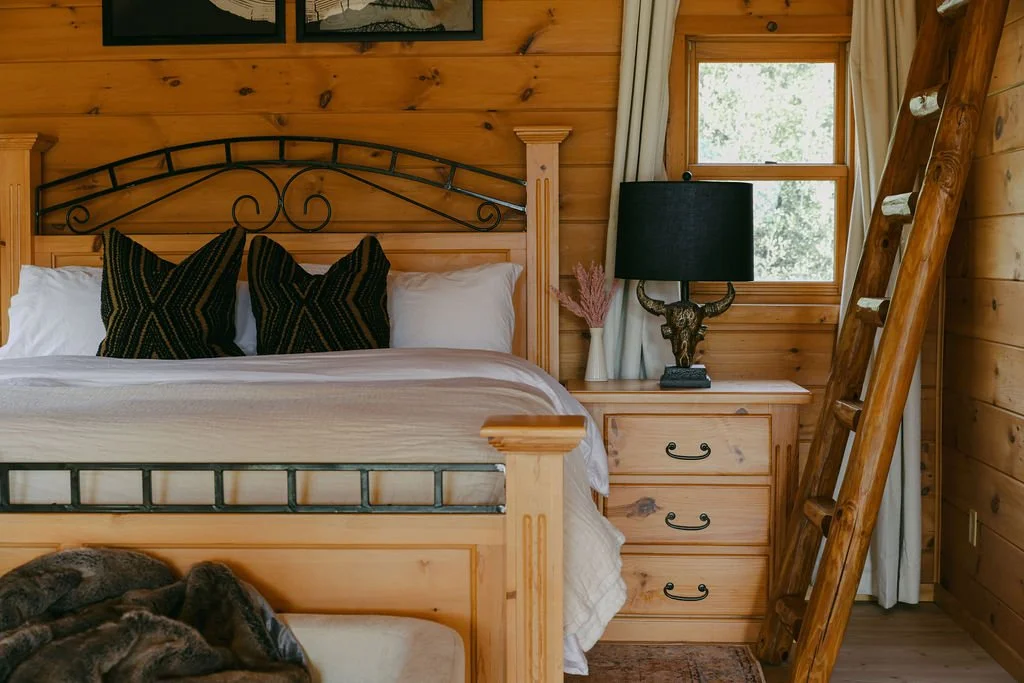 Bedroom with a wood bed, black pillows and a ladder to the loft at Dark Moon Chalet in Julian, designed by Salt and Sky Lodging Co.