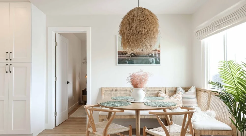 A renovated dining nook in the Oceanside apartment project, with a built-in rattan banquette, wishbone chairs and a woven pendant