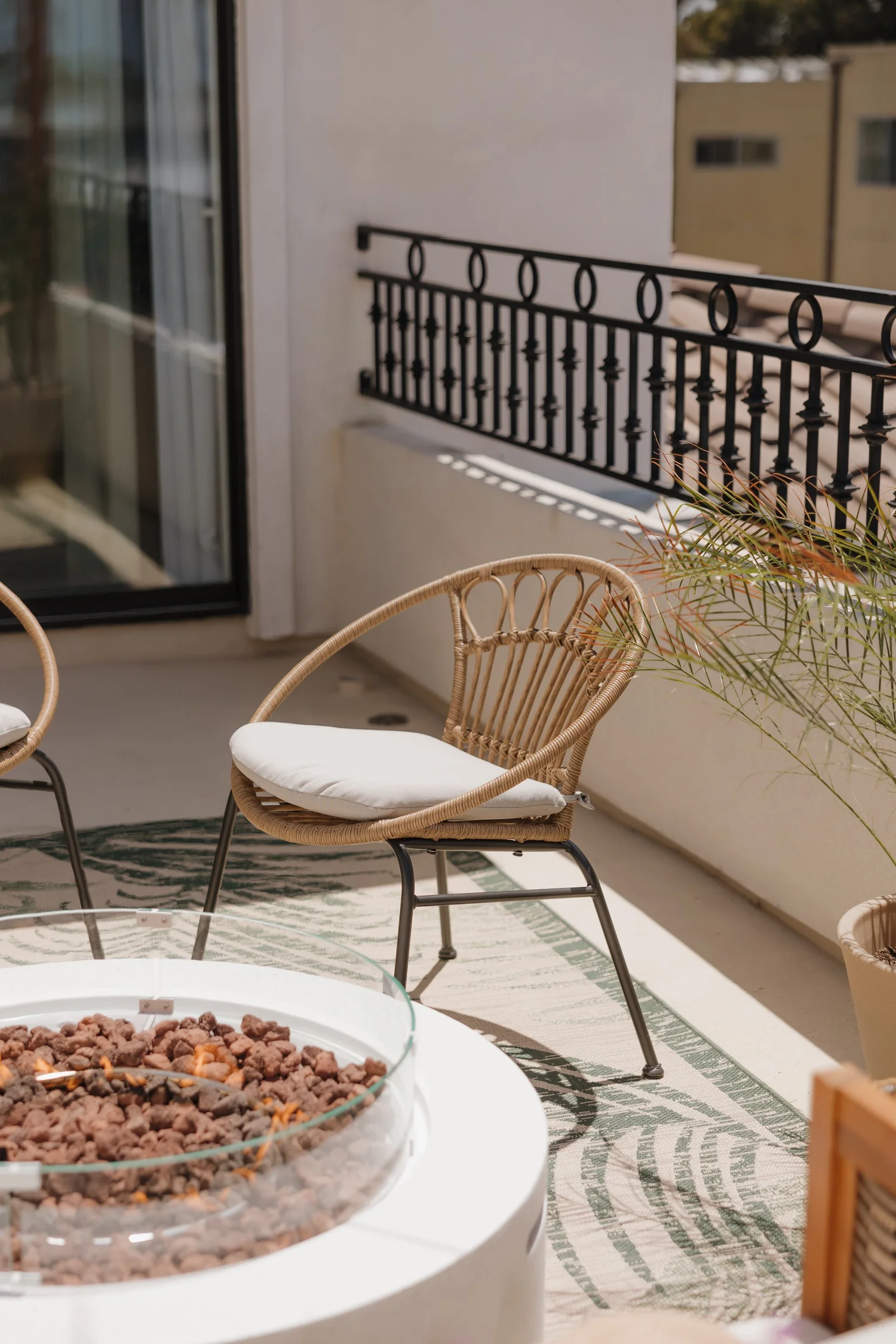 Balcony with a fire table, rattan chairs and an iron railing at Coastal Palm in Pacific Beach, designed by Salt and Sky Lodging Co.