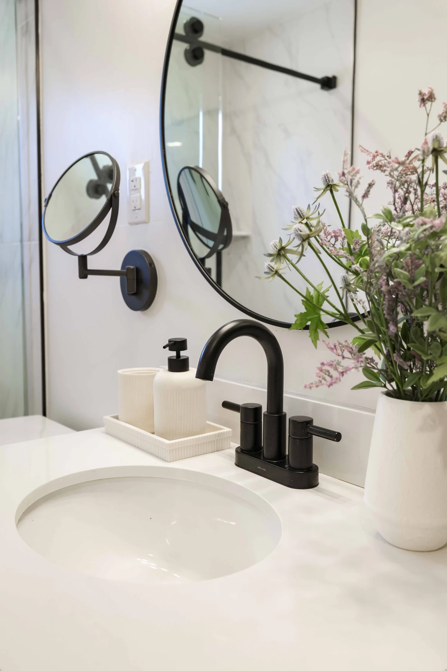 Bathroom sink with a black faucet, round mirror and flowers at Clementine A in Oceanside, designed by Salt and Sky Lodging Co.