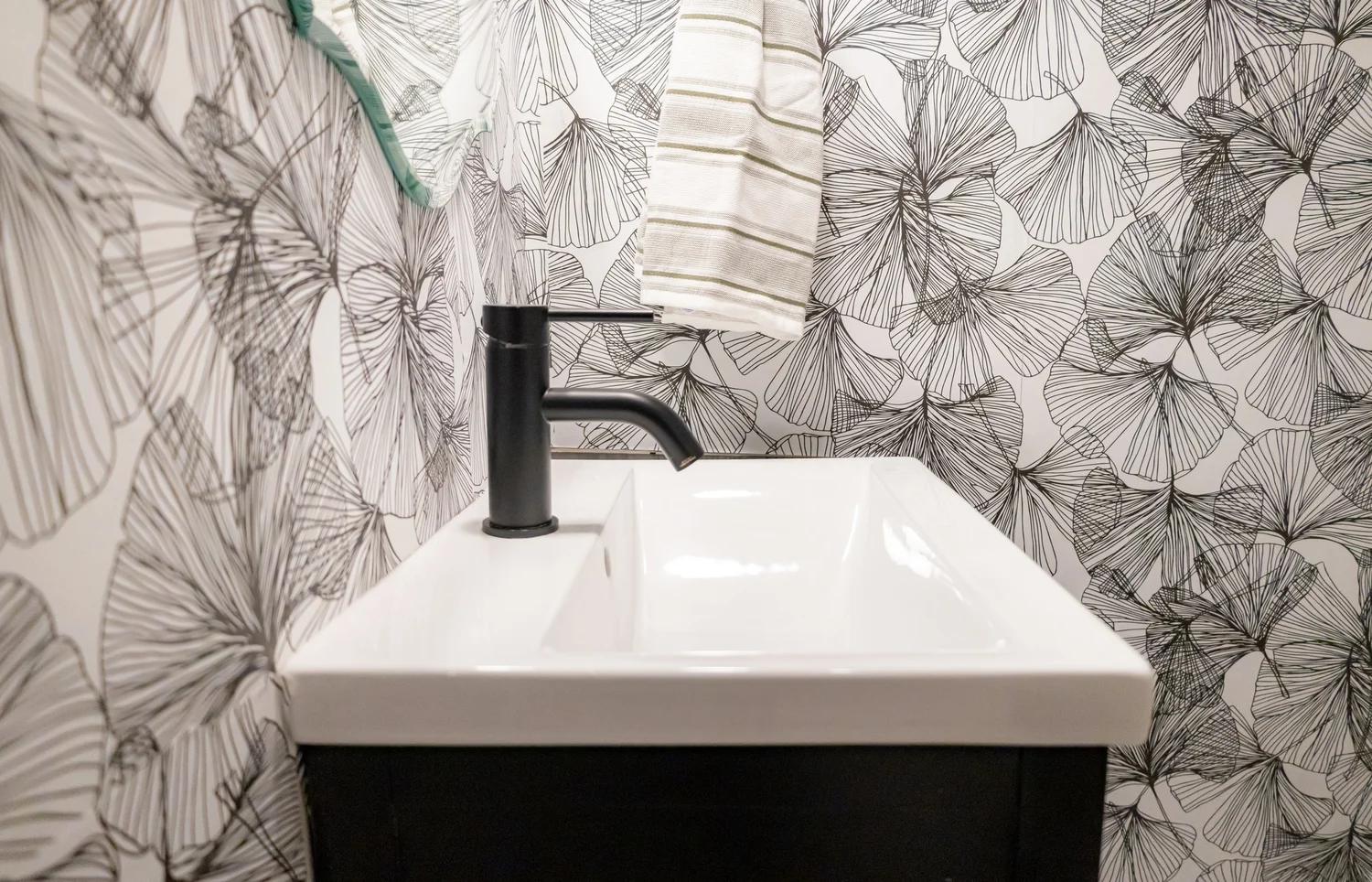 Powder room with black and white leaf wallpaper and a black faucet at Elmsgate in Birmingham, designed by Salt and Sky Lodging Co.