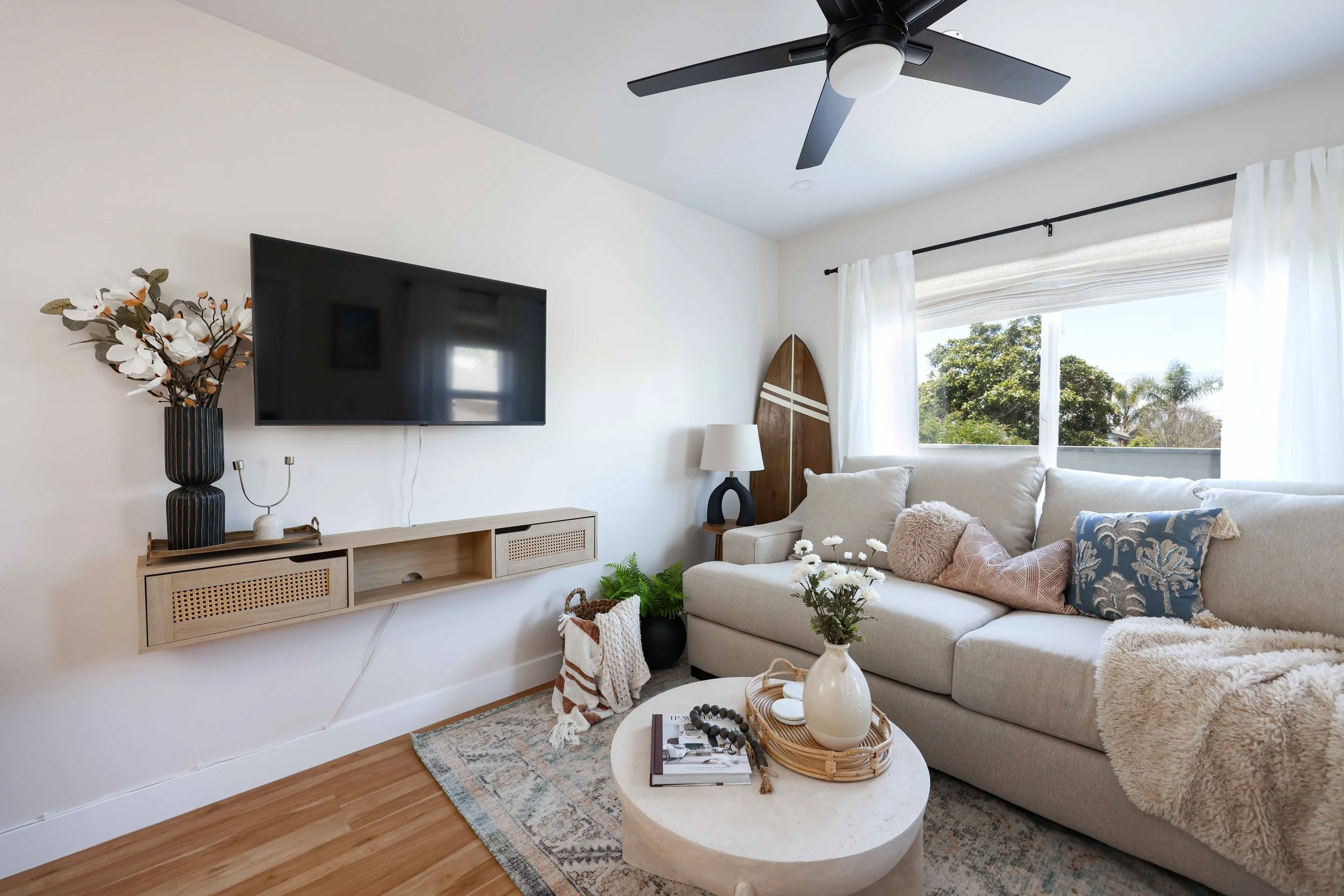 Living room with a cream sofa, floating media shelf and ceiling fan at Clementine A in Oceanside, designed by Salt and Sky Lodging Co.