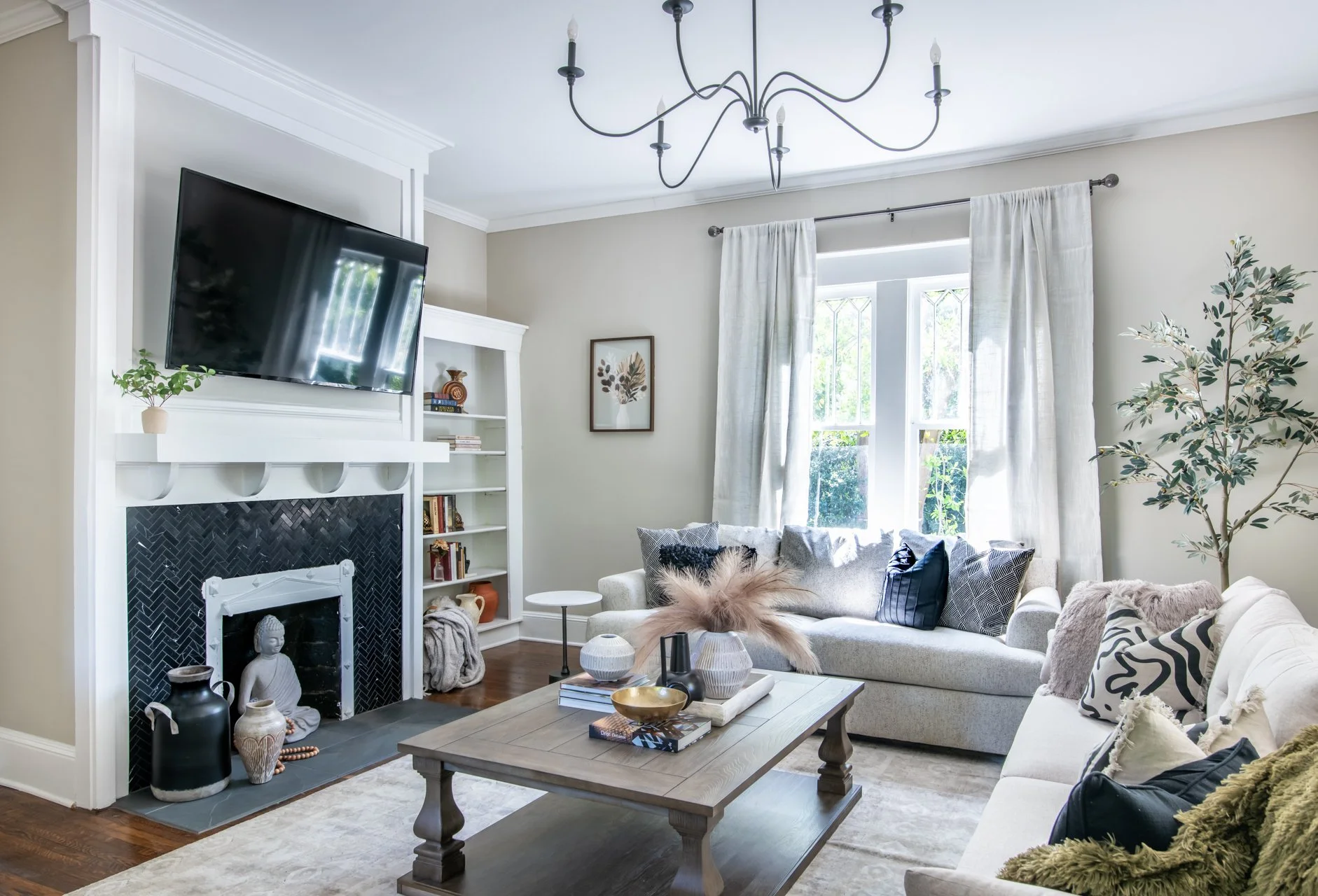 Living room with a black herringbone tile fireplace, built in shelves, an iron chandelier and leaded glass windows at Elmsgate in Birmingham, designed by Salt and Sky Lodging Co.